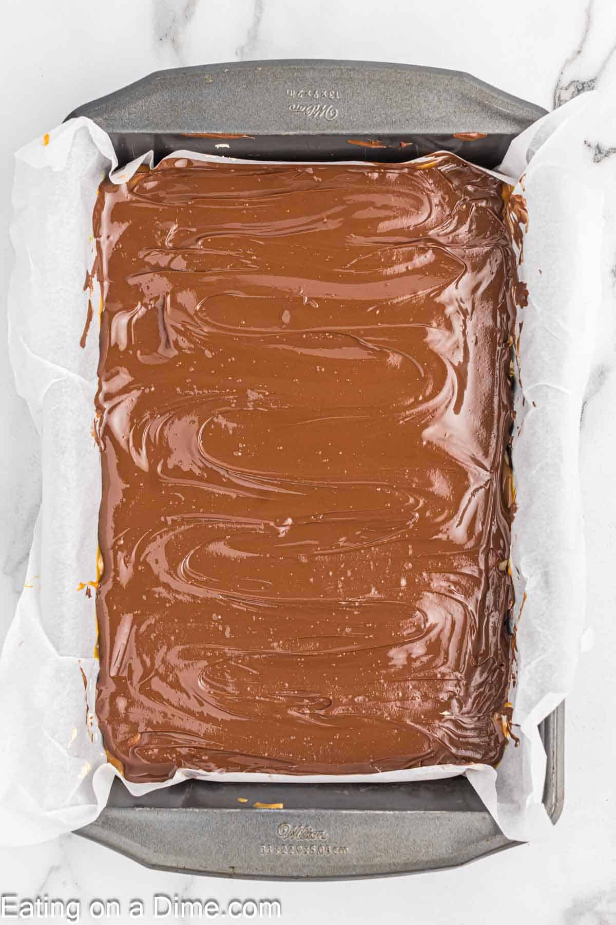 Spreading melted chocolate over caramel mixture in a baking dish