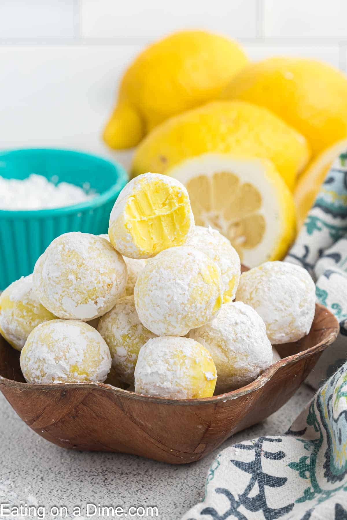 Lemon Truffles covered with powdered sugar stacked in a bowl with fresh lemon in the background