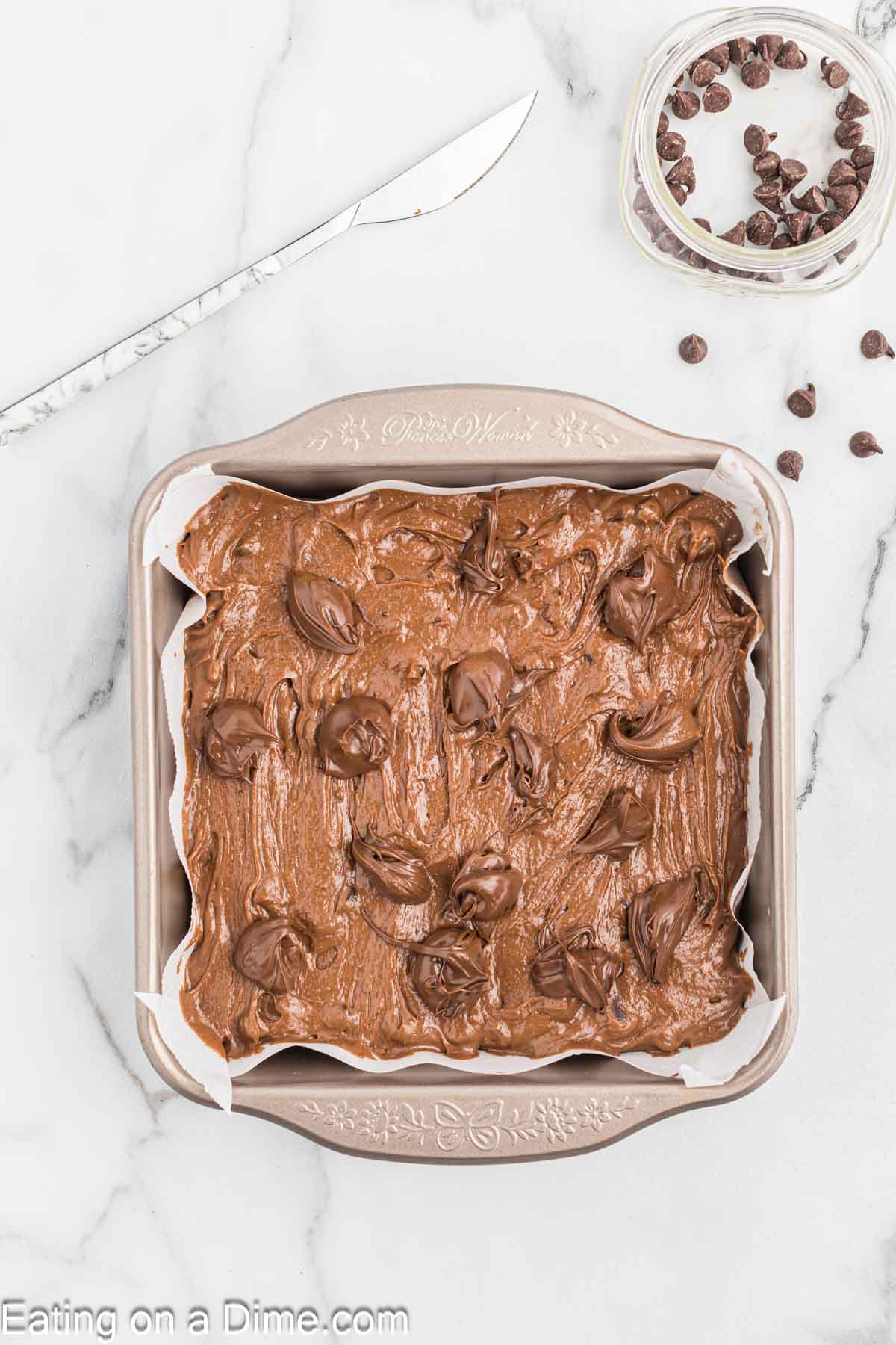 Dollops of Nutella are placed on brownie batter in a baking dish