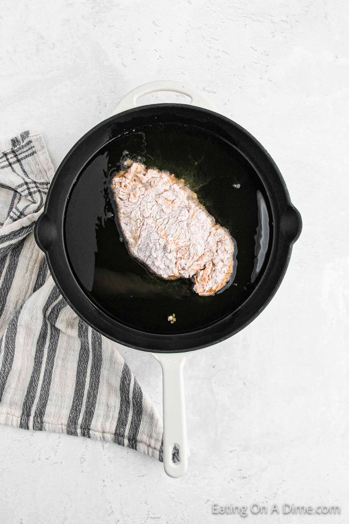 Placing the flour covered chicken breast in a cast iron skillet with oil