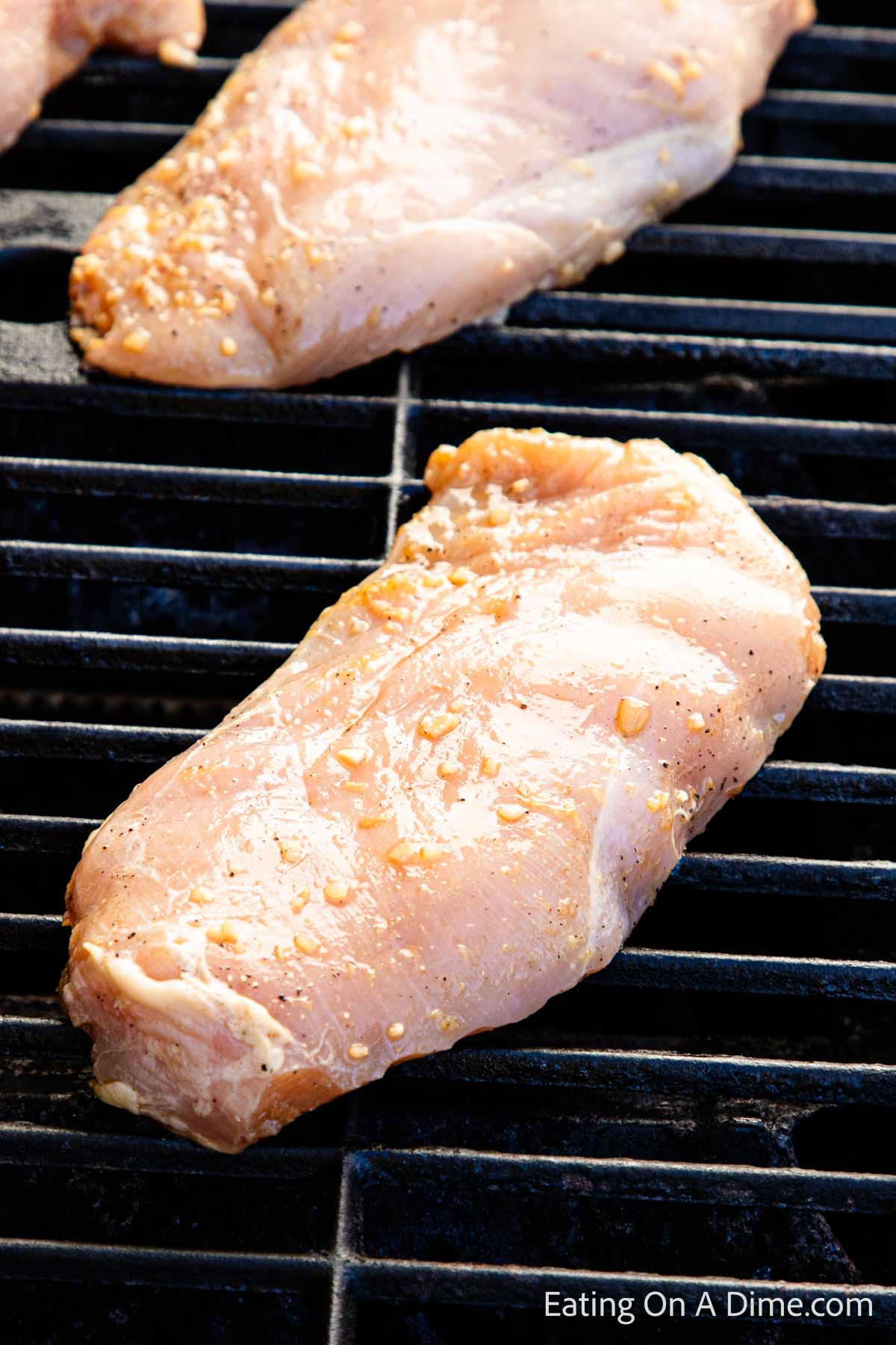 Placing marinated chicken breast on a grill grates