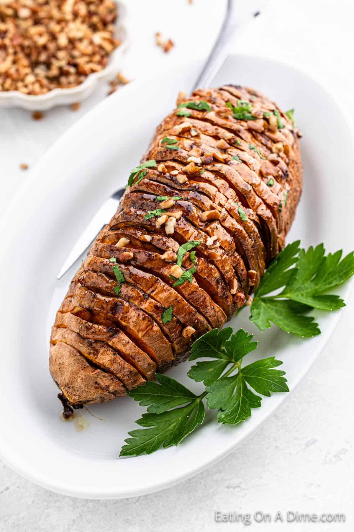 Hasselback Sweet Potatoes on a plate topped with chopped pecans 