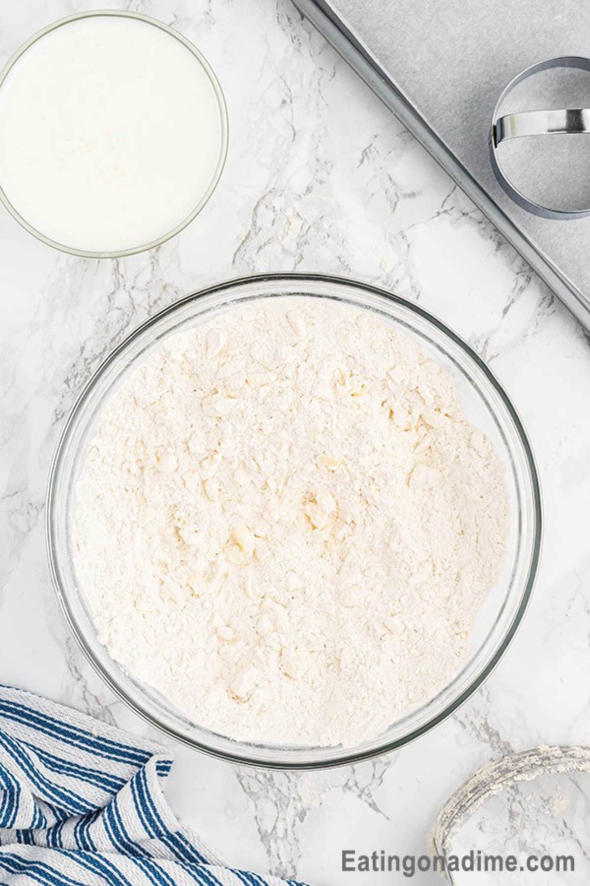 A bowl of buttermilk on the side of flour mixture with mixed in butter
