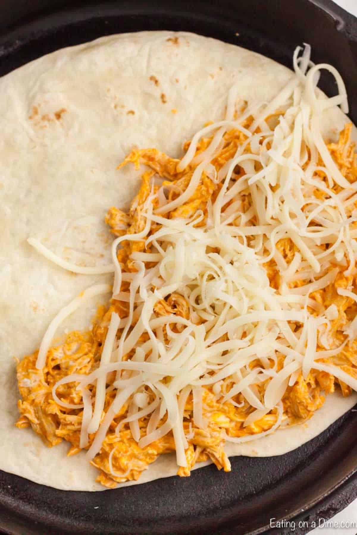 Flour tortilla in a skillet topped with buffalo chicken mixture and shredded cheese