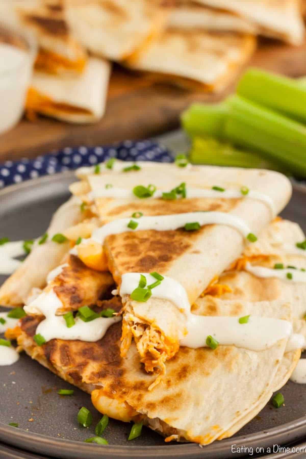 Buffalo chicken quesadilla cut into triangle topped with sour cream and chopped green onions