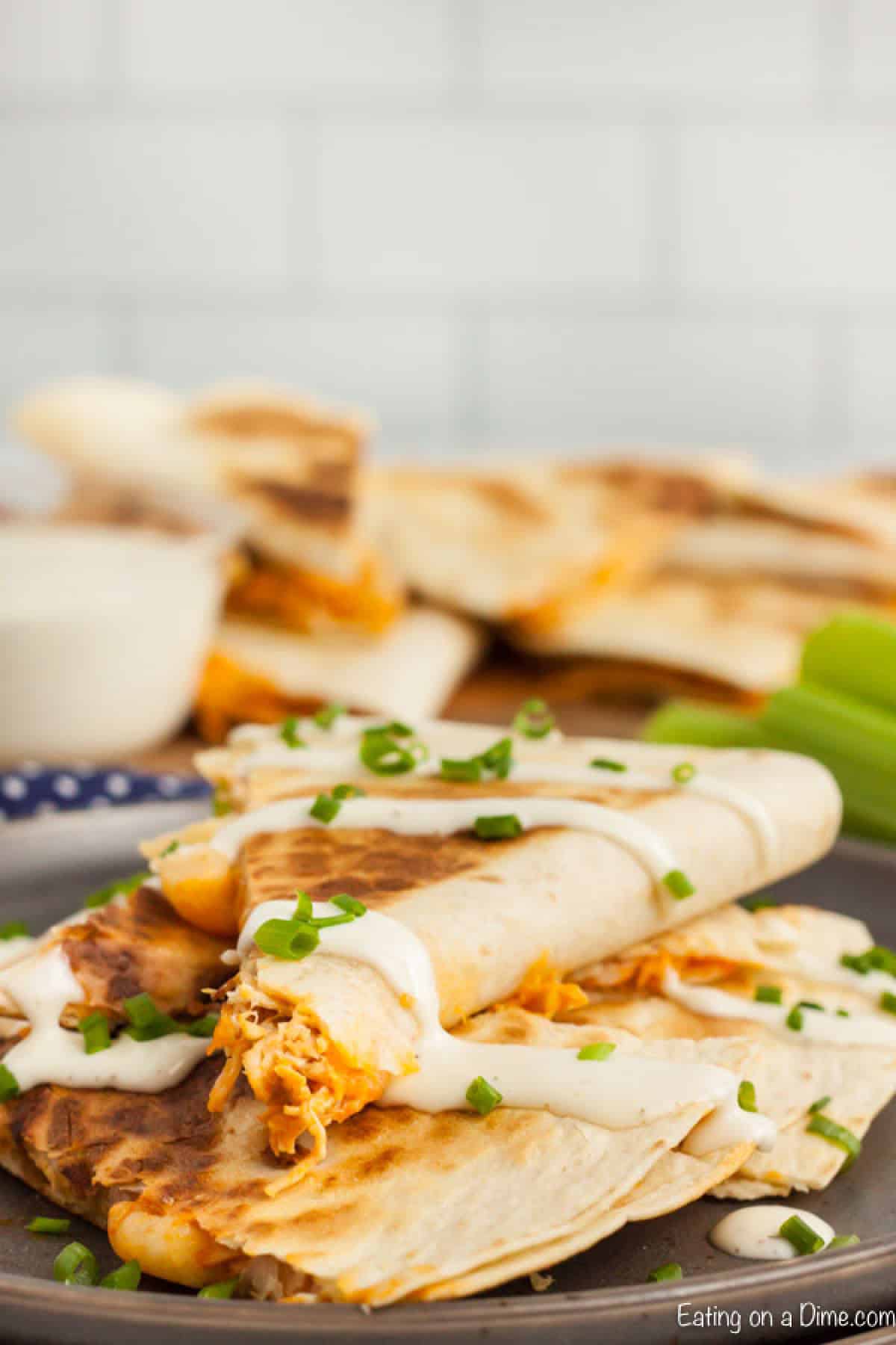 Buffalo Chicken Quesadillas stacked on a plate with sour cream drizzled on top with chopped green onions