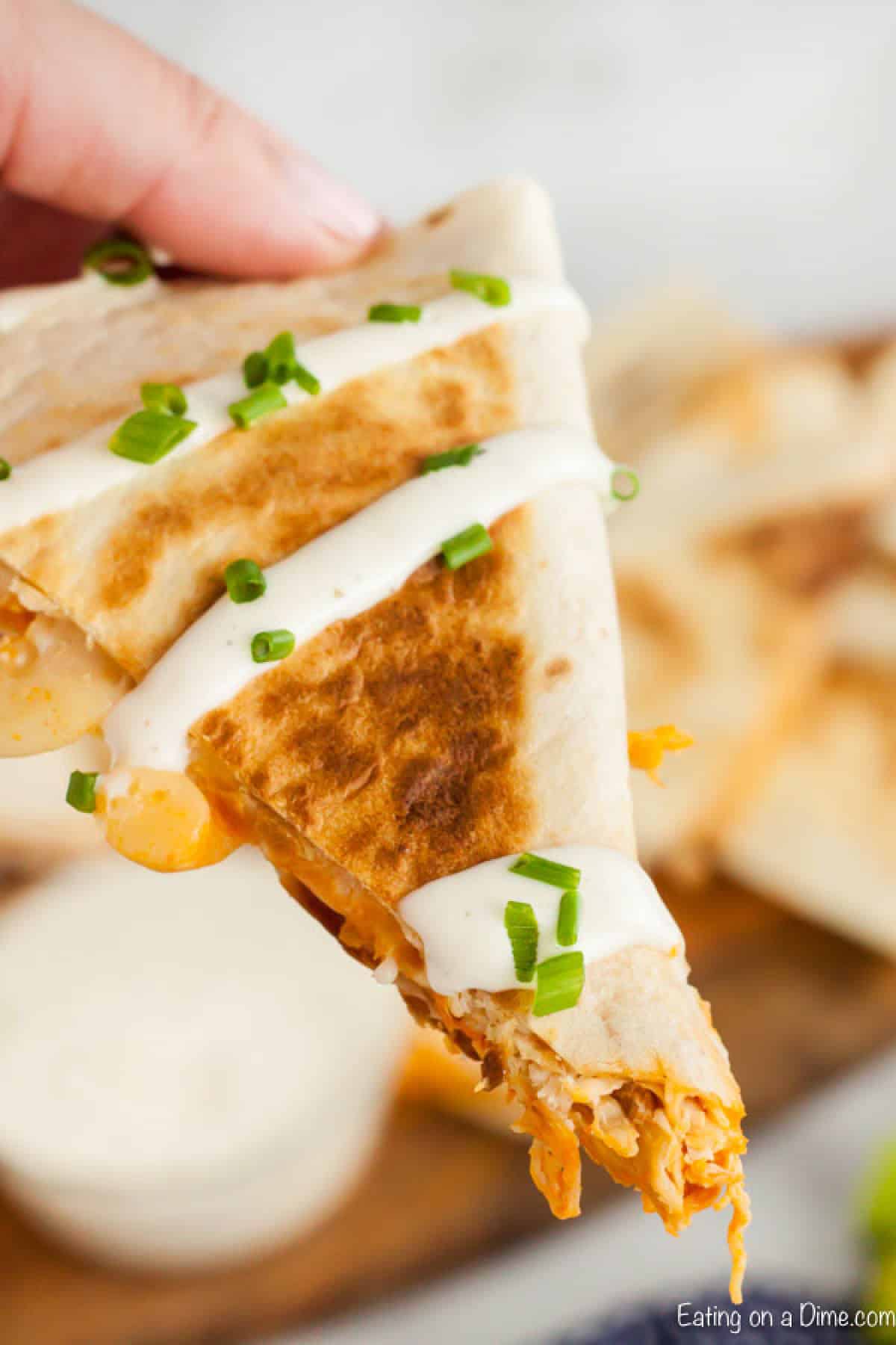 Buffalo Chicken Quesadilla cut into a triangle topped with sour cream and chopped onions