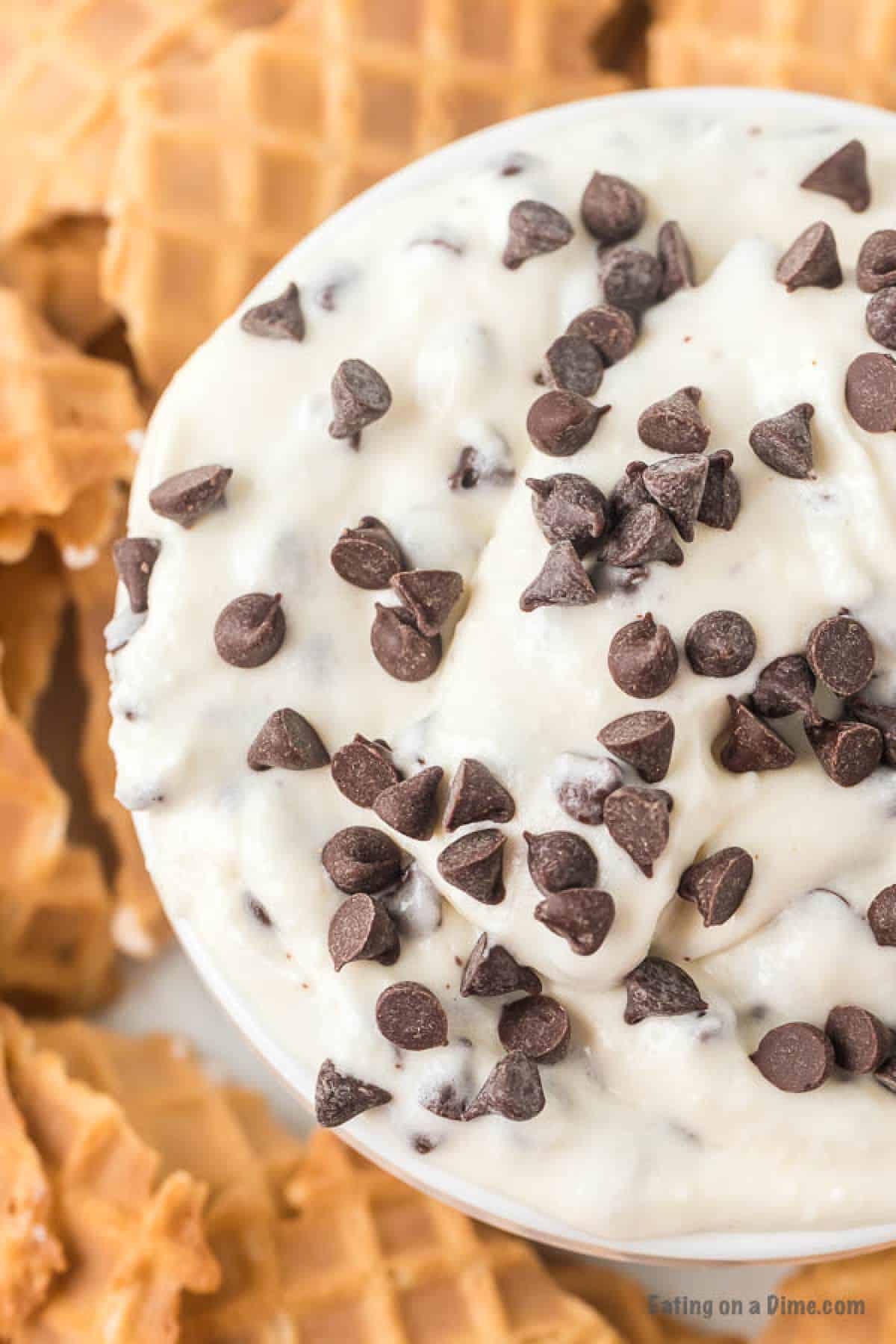 Cannoli Dip in a bowl topped with chocolate chips with piece of cone in the background