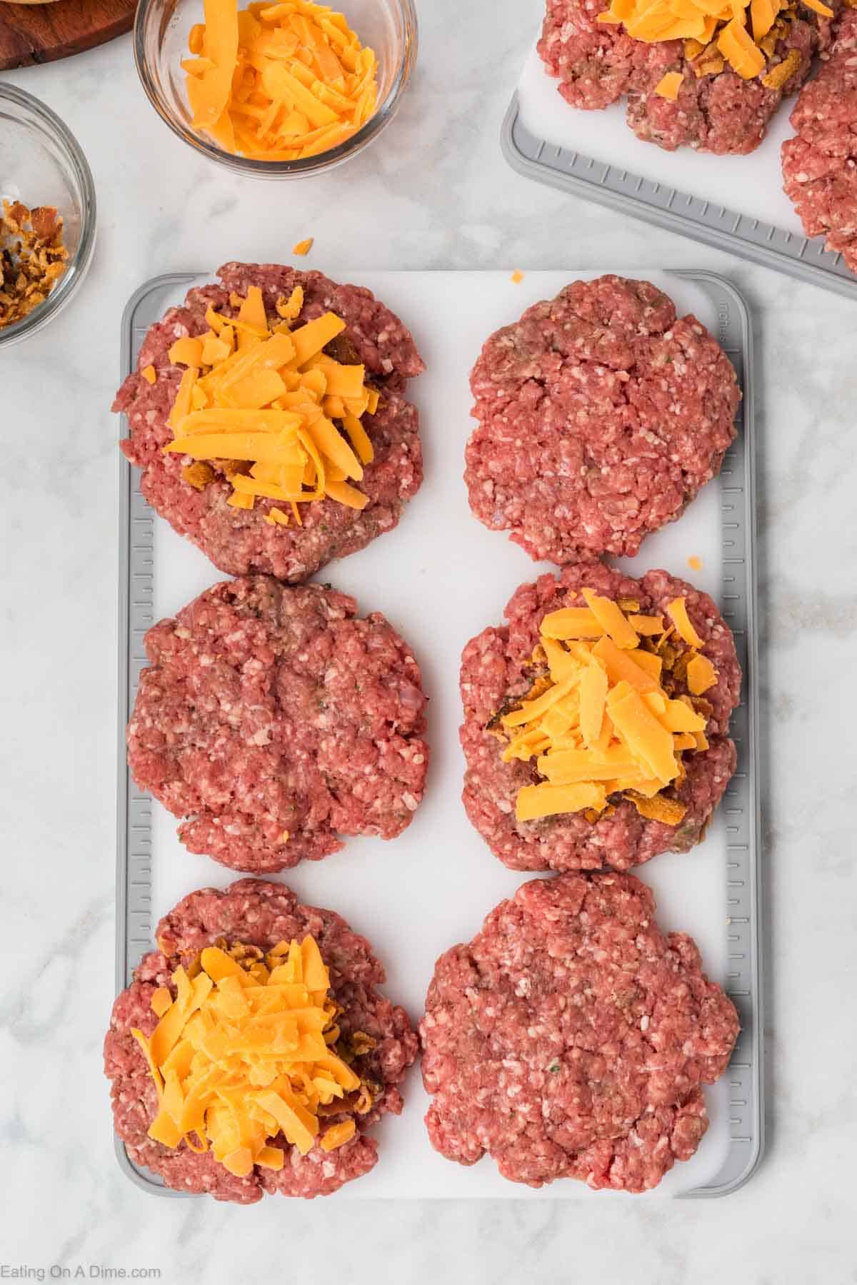 Shredded Cheese on top of ground beef patties on a cutting board