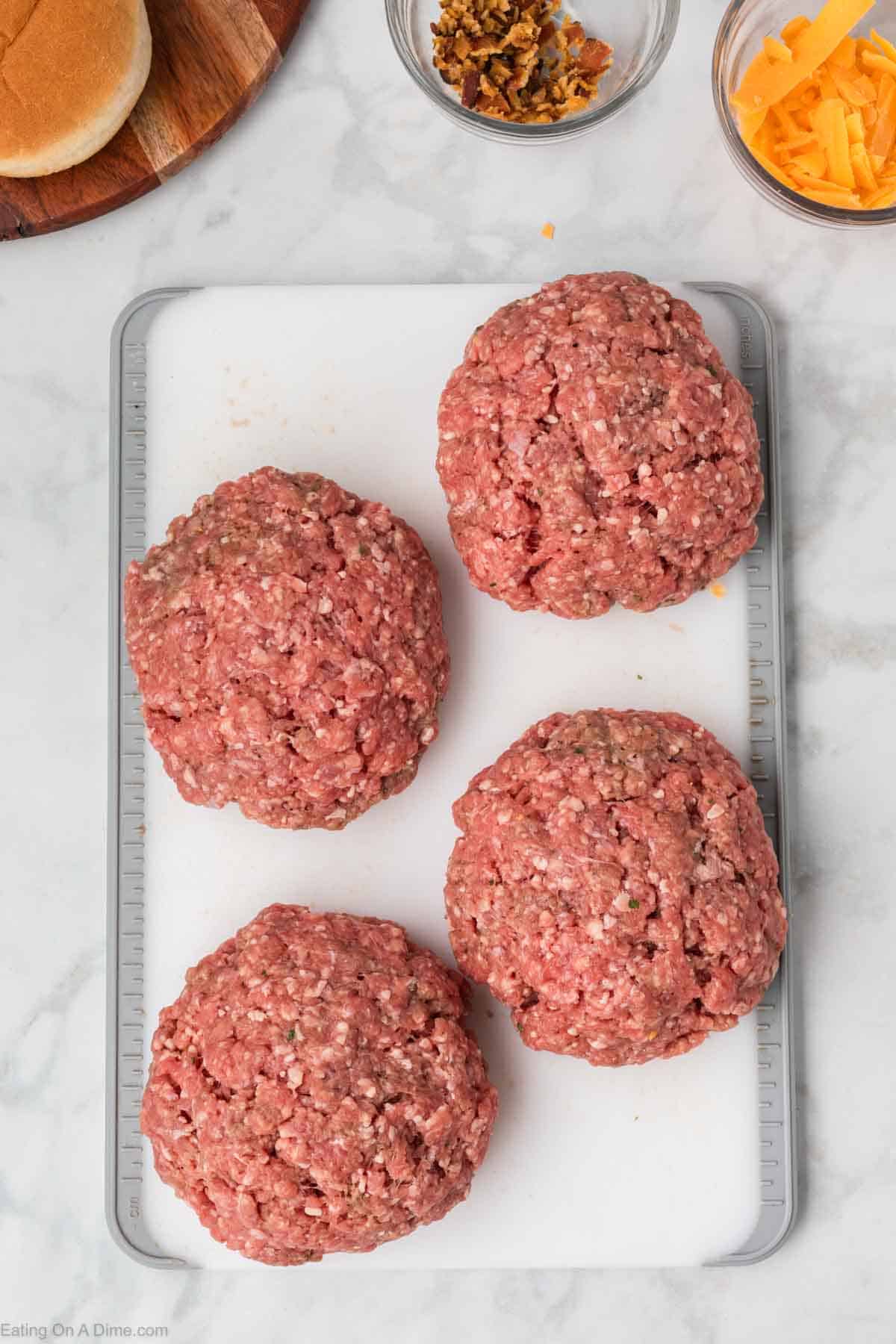 4 large ground beef patties on a cutting board