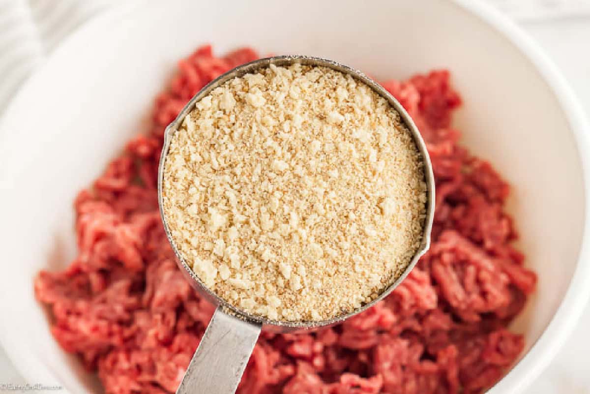 Ground beef in a bowl with a measuring cup full of breadcrumbs