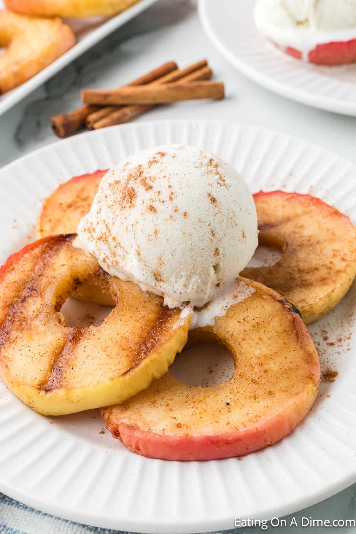 Sliced Grilled Apples on a plate topped with a scoop of ice cream and cinnamon