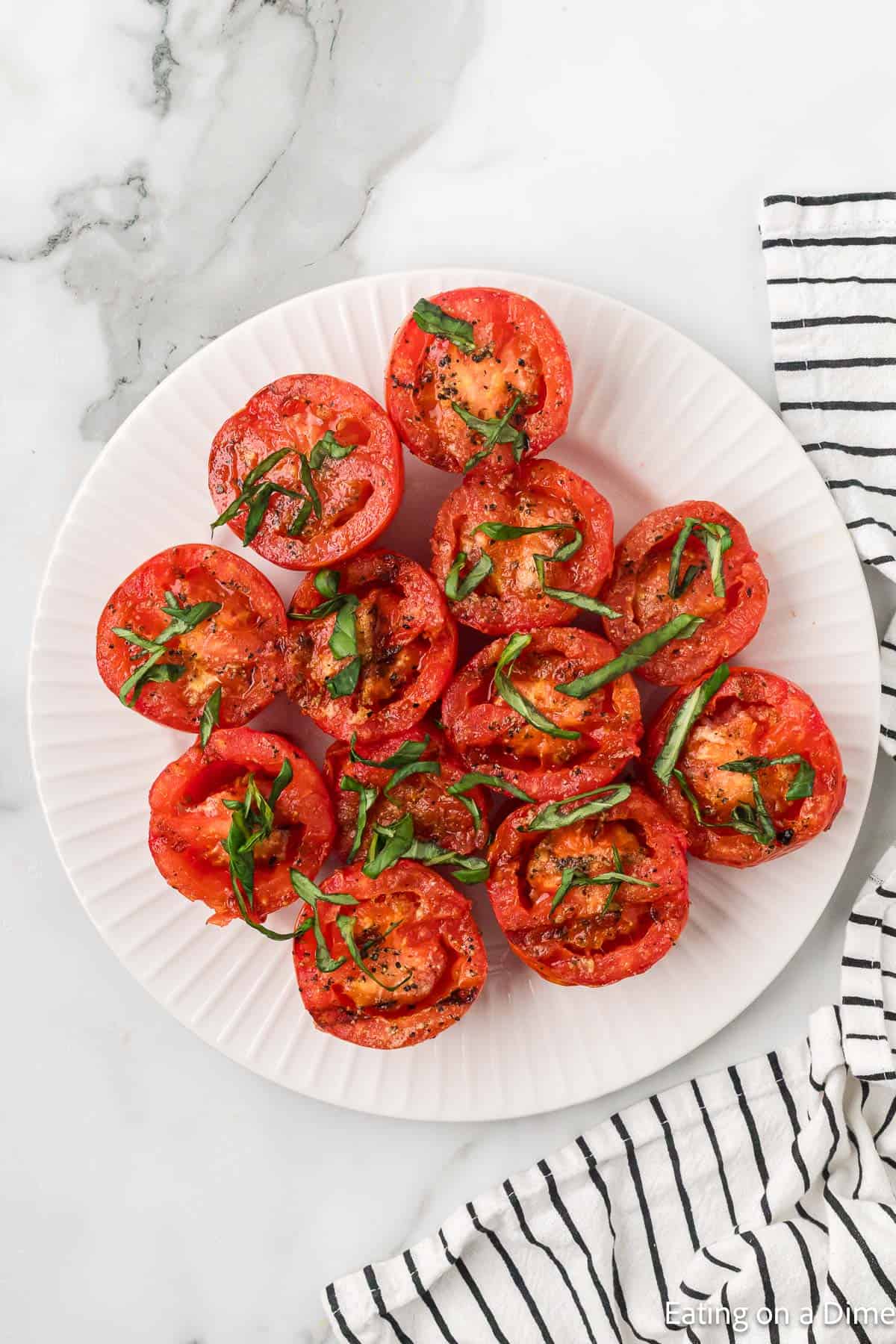 Grilled tomatoes halves on a plate topped with fresh basil