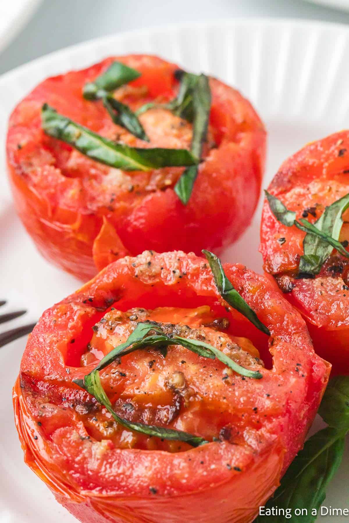 Sliced grilled tomatoes on a plate topped with fresh basil strips