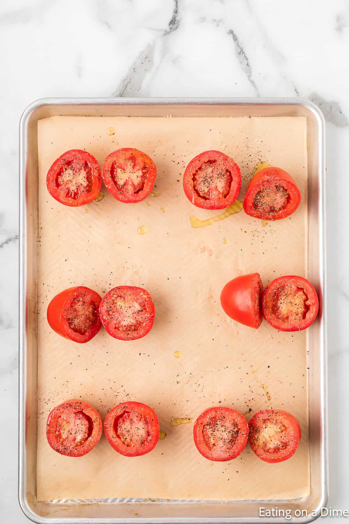 Slice Roma Tomatoes on a baking sheet lined with parchment paper topped with seasoning and oil