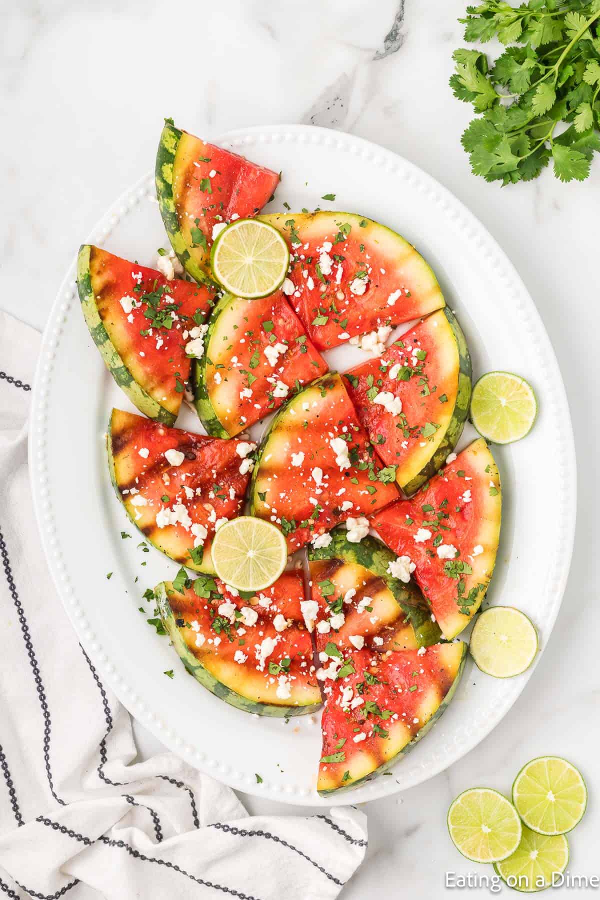 Grilled watermelon on a platter topped with feta cheese, cilantro and lime