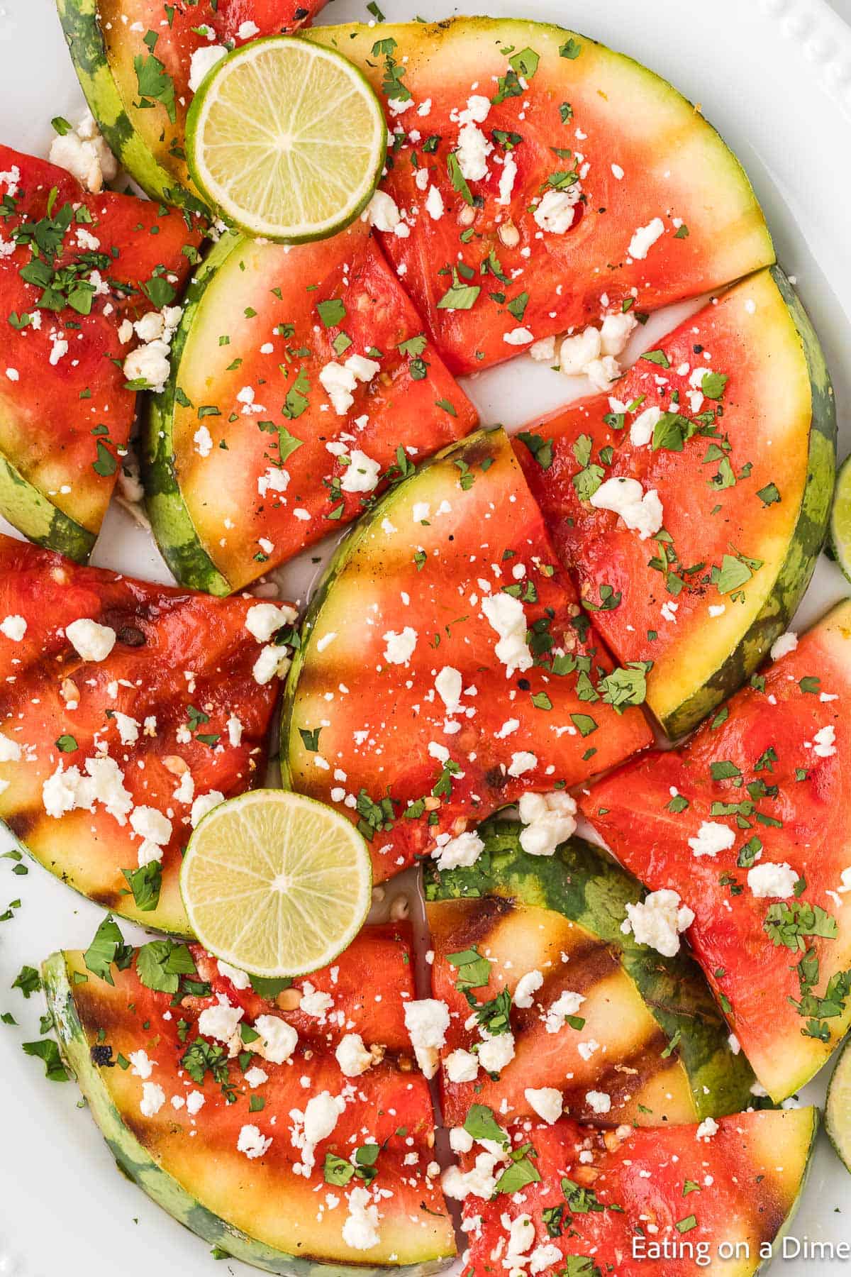 Grilled watermelon on a platter topped with feta cheese, chopped cilantro and fresh lime