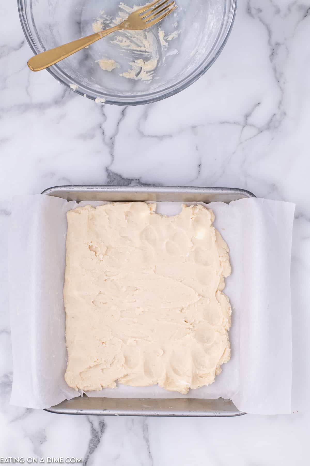 Shortbread dough pressed in a baking dish lined with parchment paper