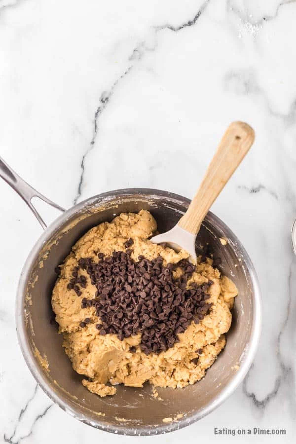 Peanut butter mixture in a saucepan topped with chocolate chips with a wooden spoon