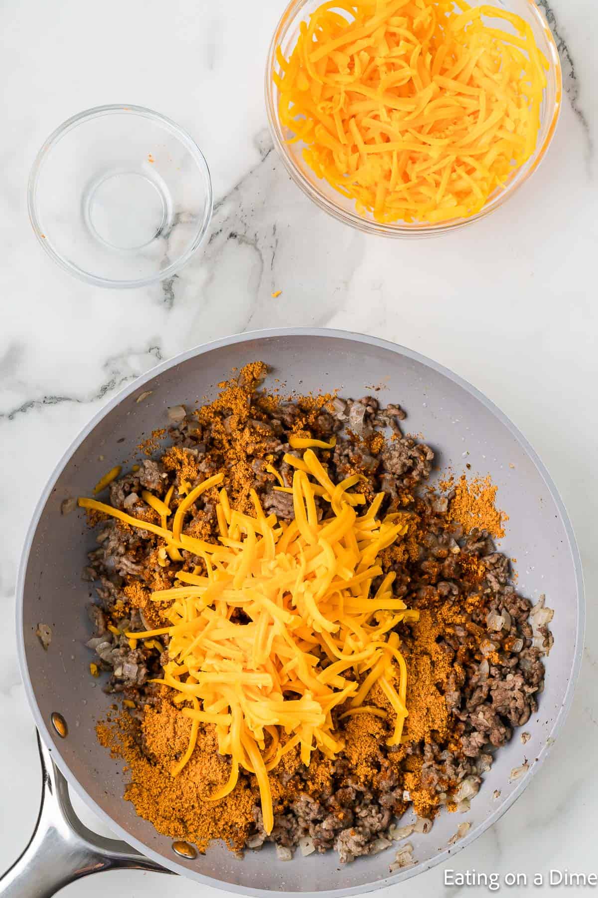 Cooked ground beef in a skillet topped with taco seasoning and shredded cheese