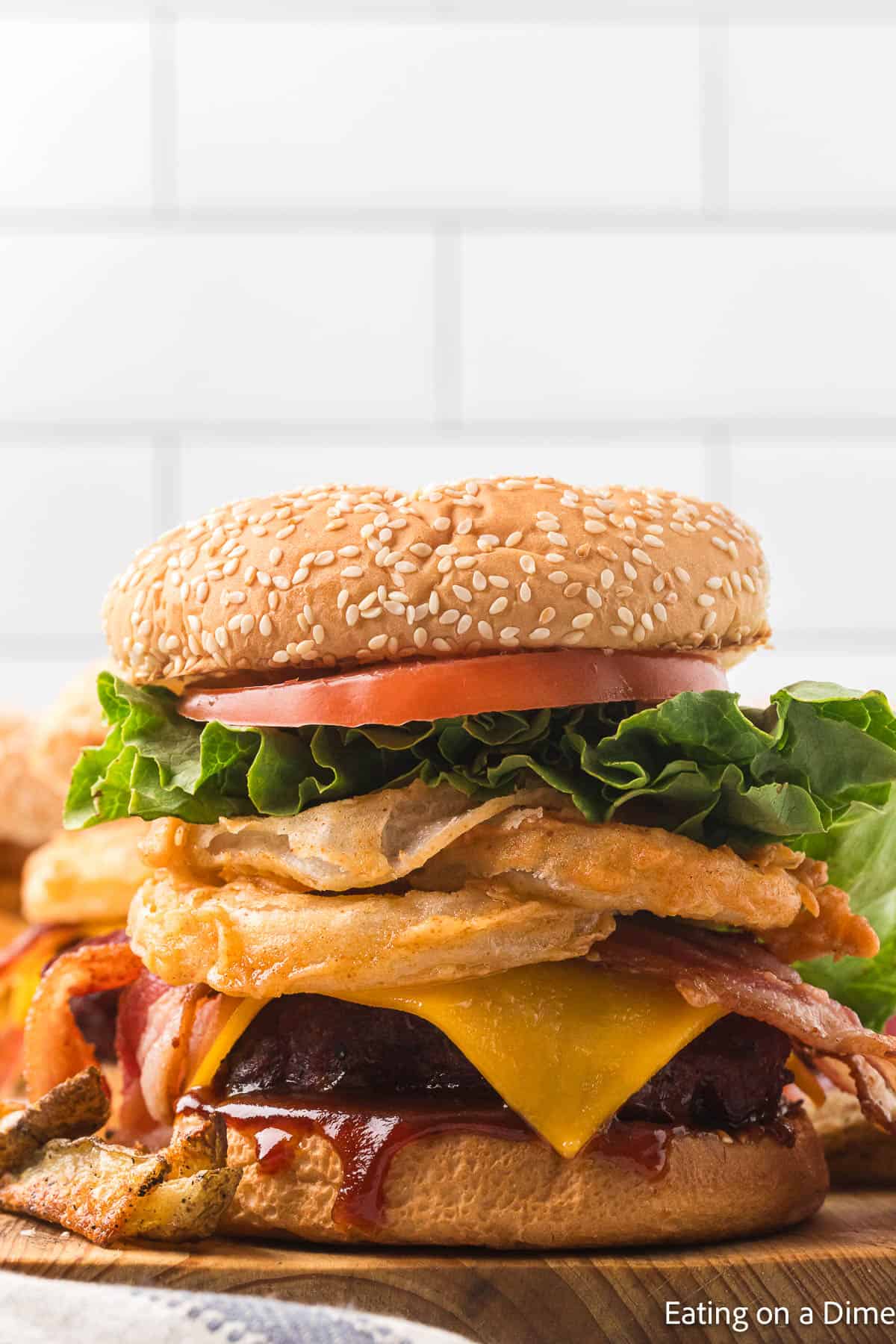 Hamburger that has slice tomato, green lettuce, crispy onion rings, bacon slices, slice of cheese and hamburger beef patties and BBQ Sauce all between seeded hamburger buns