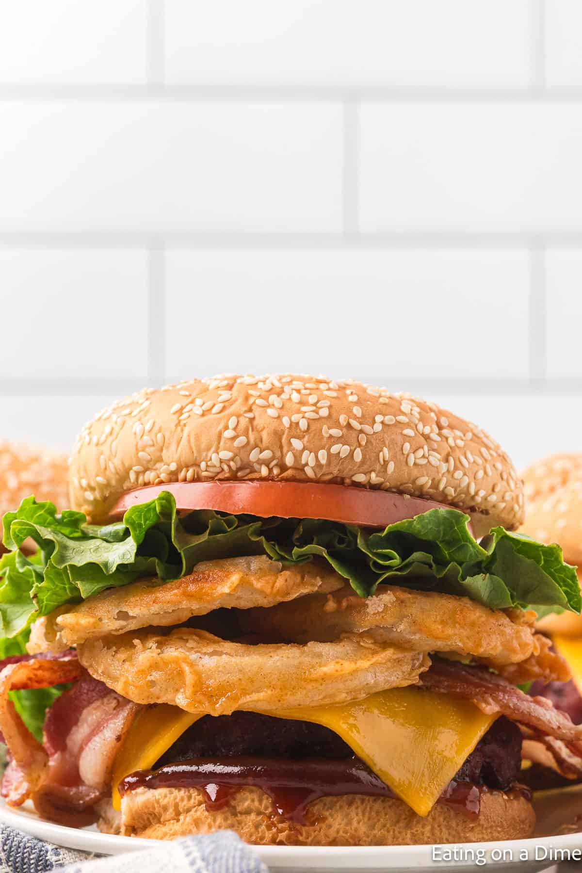 Hamburger that has slice tomato, green lettuce, crispy onion rings, bacon slices, slice of cheese and hamburger beef patties and BBQ Sauce all between seeded hamburger buns