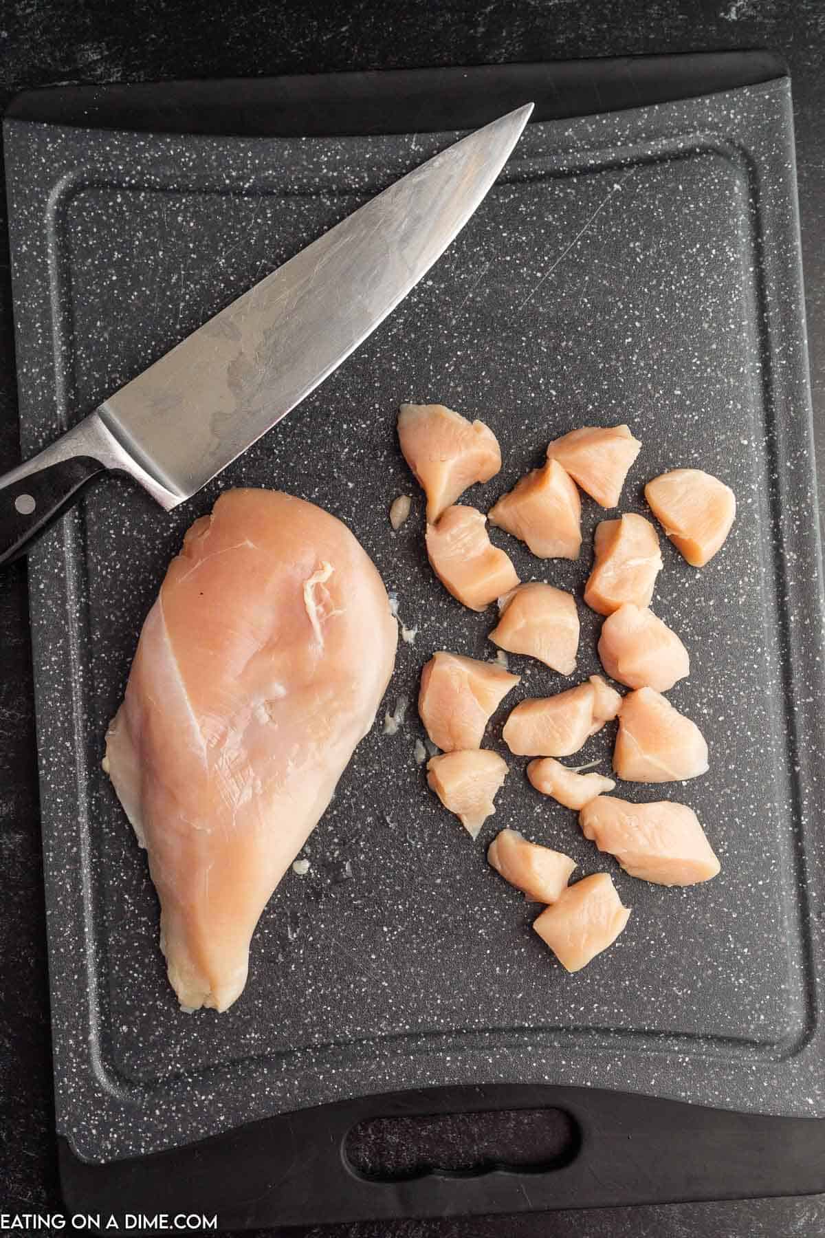 Cut chicken breast in bite size pieces on a cutting board with a knife