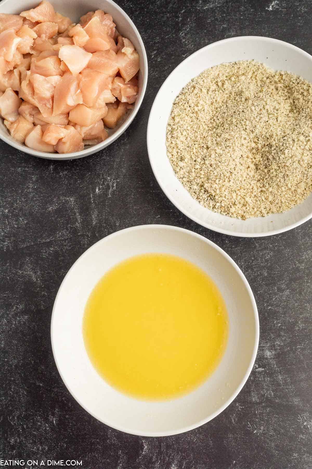 Melted butter in a bowl, a bowl of bread crumb mixture and a bowl of bite size chicken