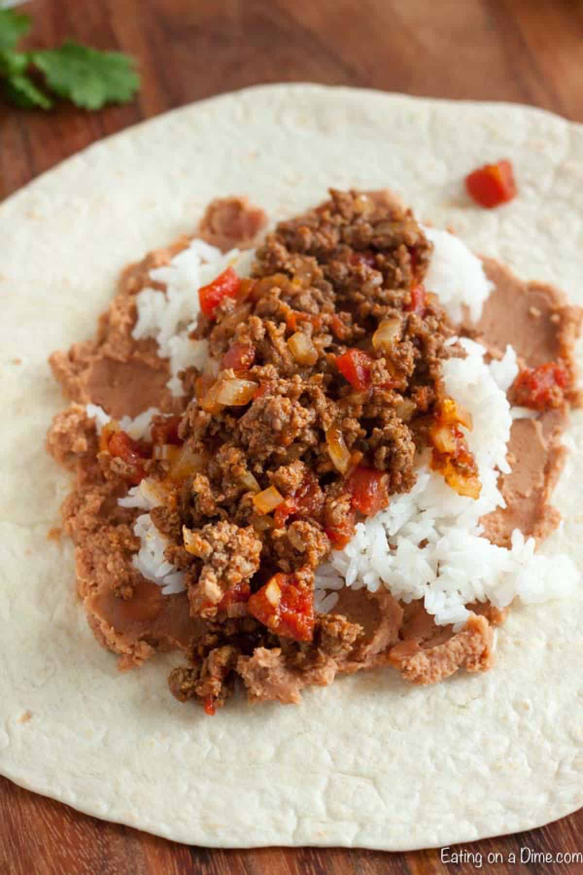 Flour tortilla topped with refried beans, white rice, ground beef mixture