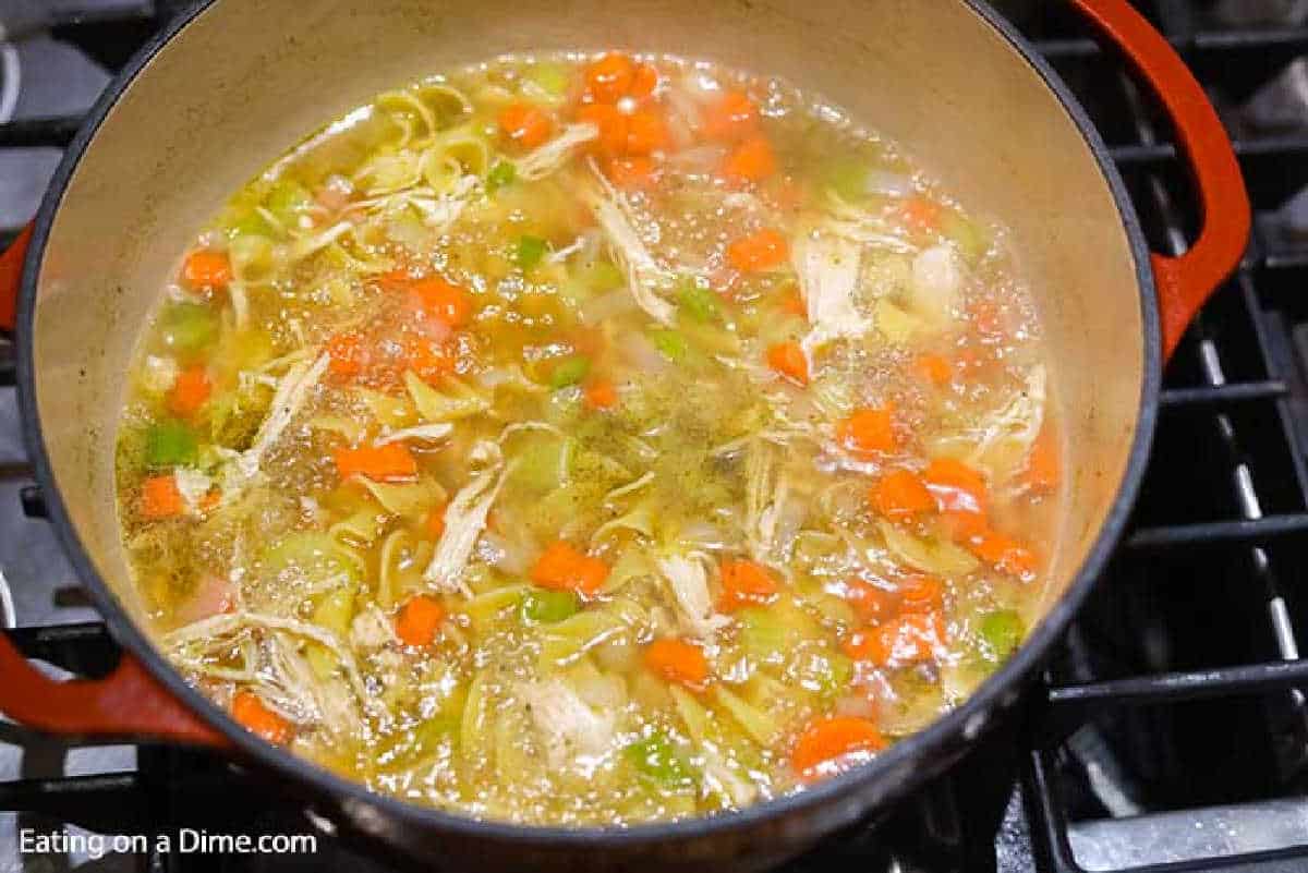 Adding broth and cooked chicken to the large pot with the carrots, celery, and onion