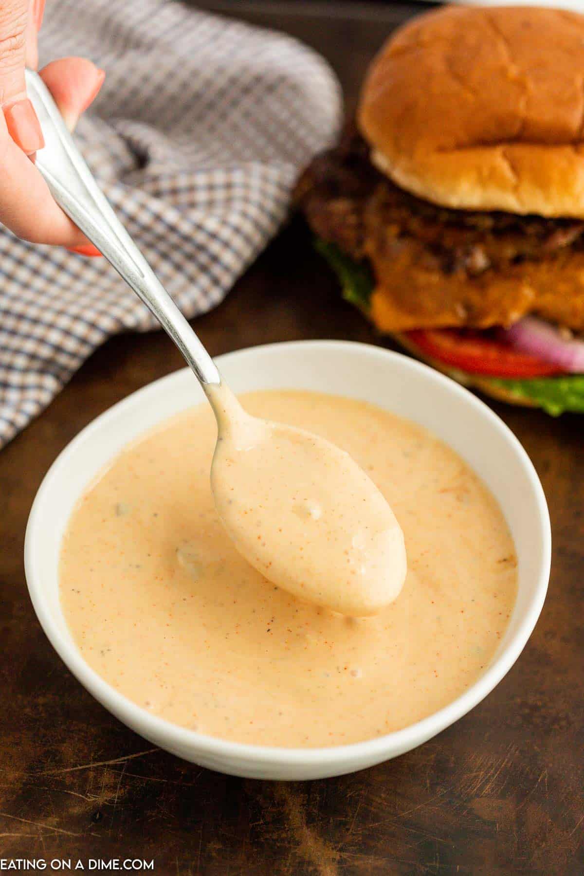 Burger Sauce in a bowl with a serving on a spoon with a burger in the background