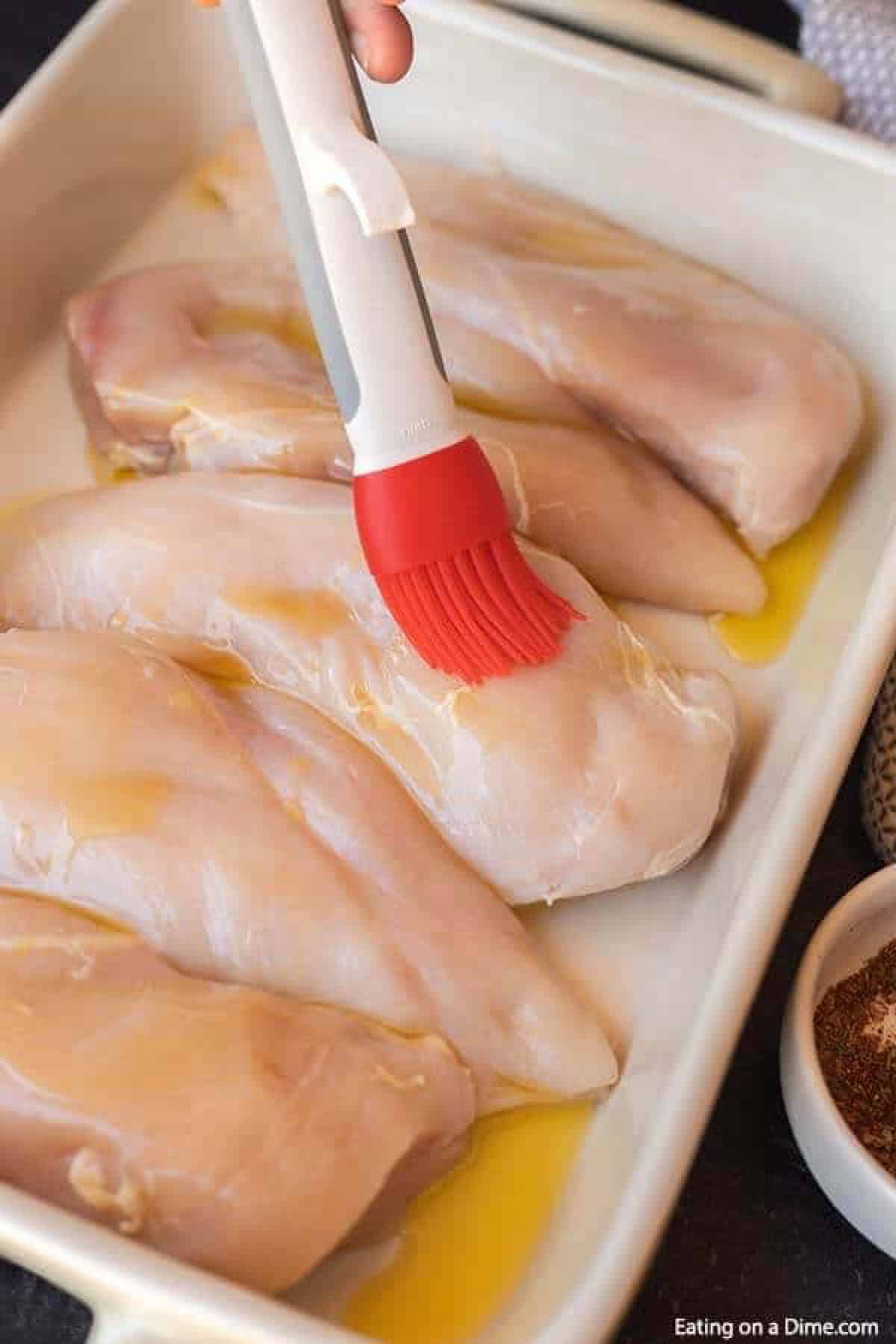 Brushing oil on chicken breast in a baking dish