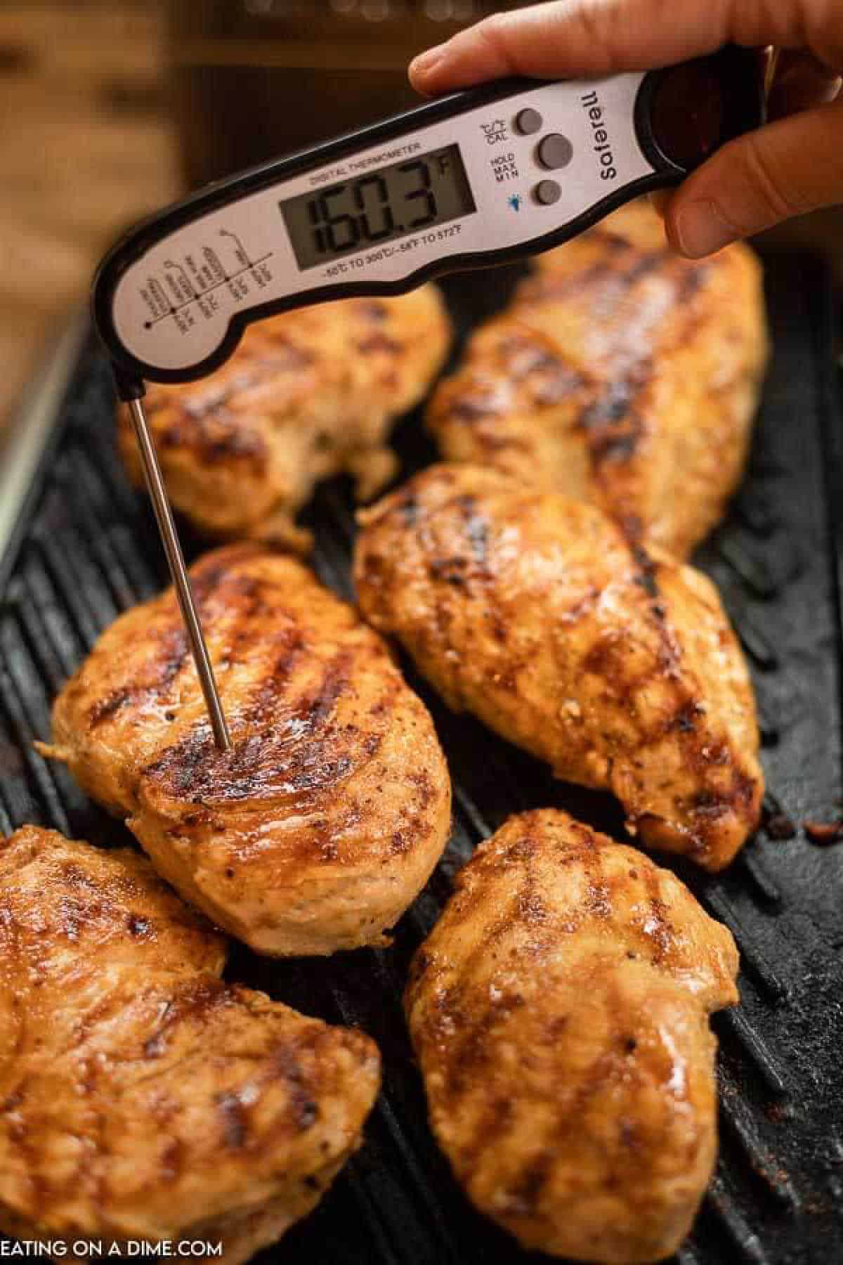 Chicken breasts on a grill with a meat thermometer entered into one chicken breasts with a reading of 160.3 degrees F. 