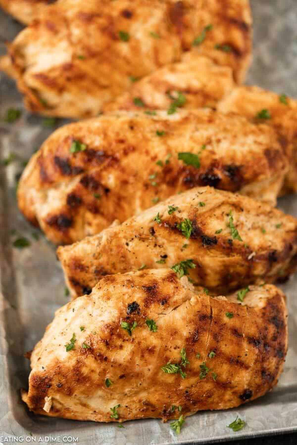 5 grilled chicken breasts on a silver platter topped with fresh chopped parsley. 