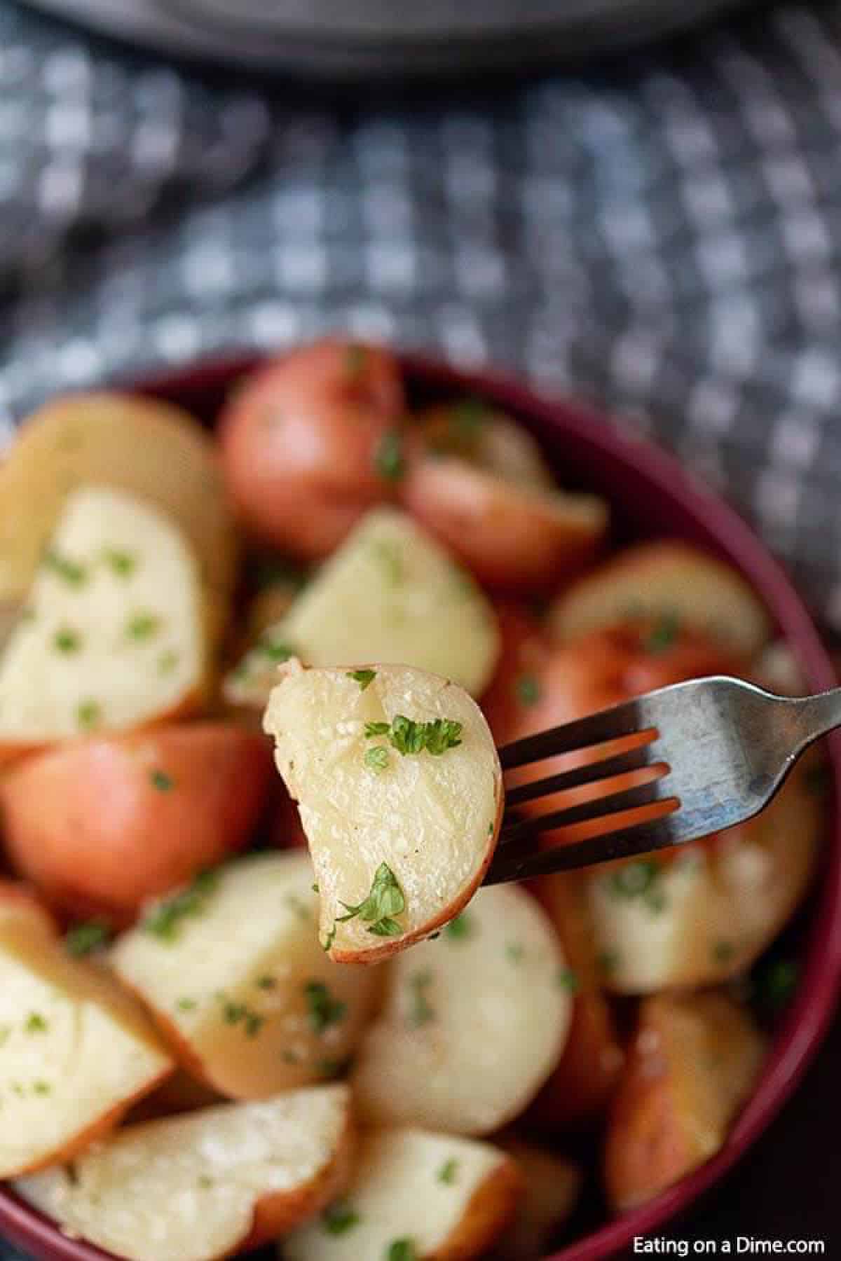 Cooked instant pot red potatoes in a large red bowl topped with fresh parsley and a fork with 1 of the potatoes on them 