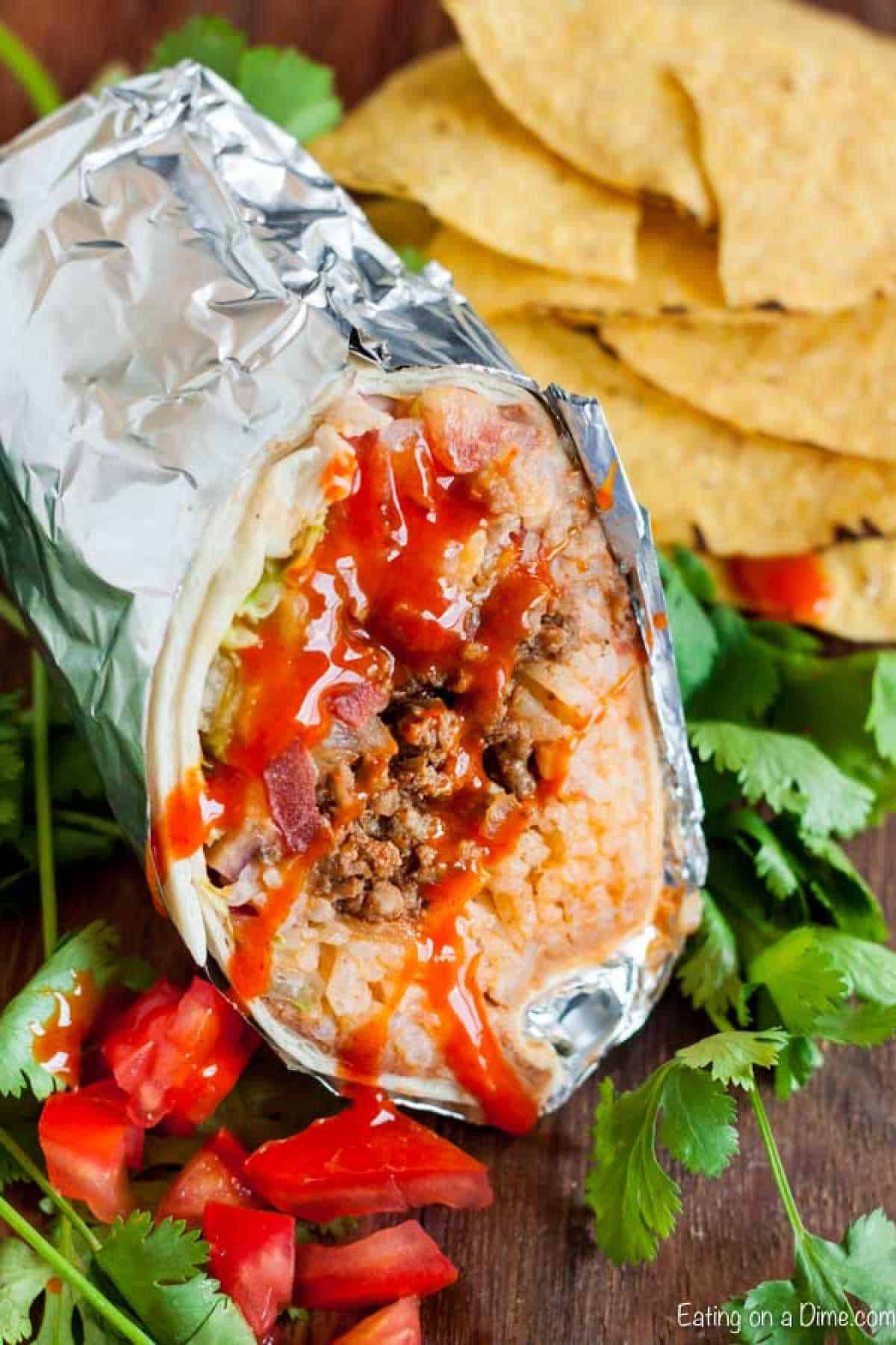 Burrito wrapped in foil cut in half and loaded with beef, white rice, Rotel and melted cheese with a side of tortilla chips