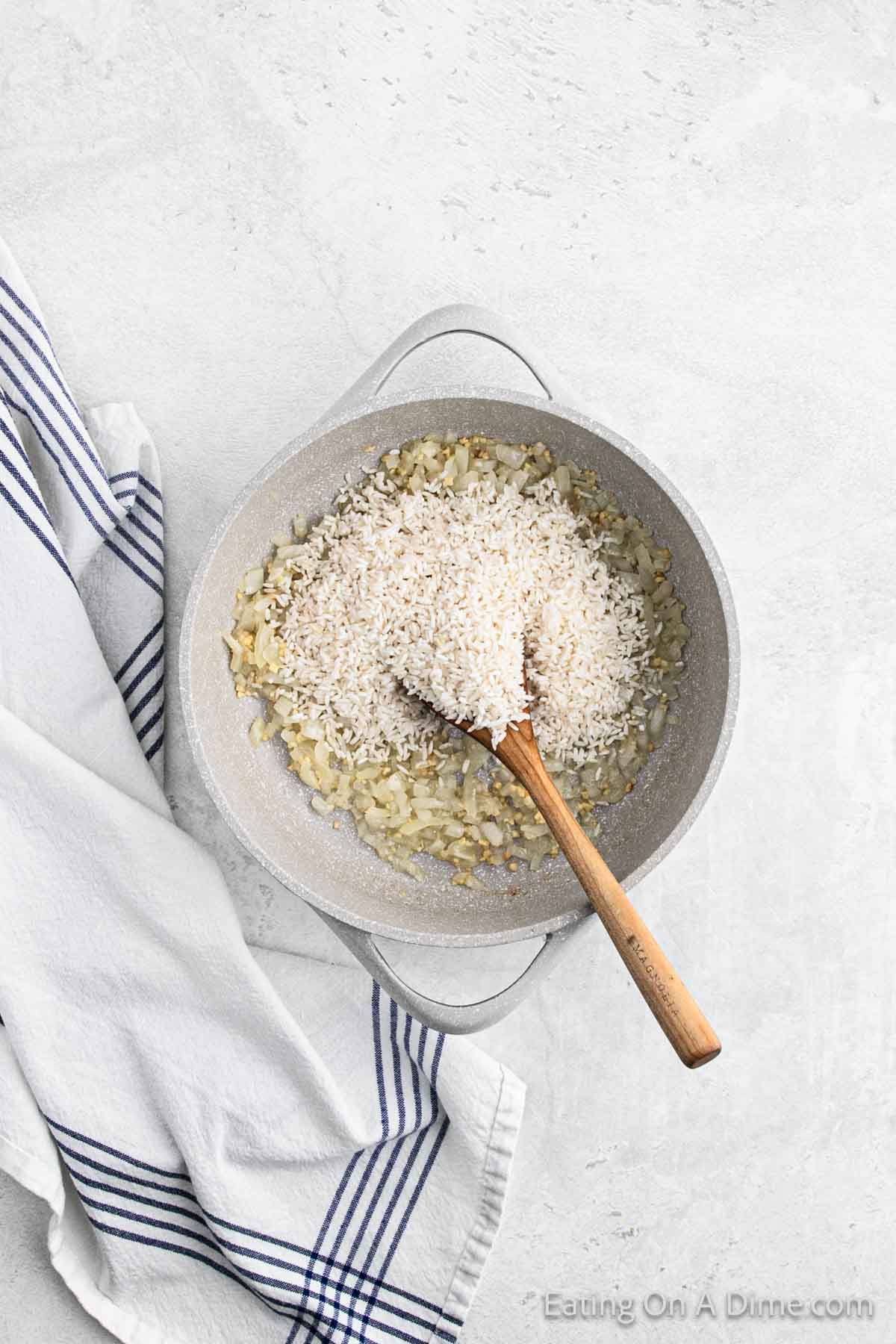 Adding the rice to the large skillet with the chopped onions