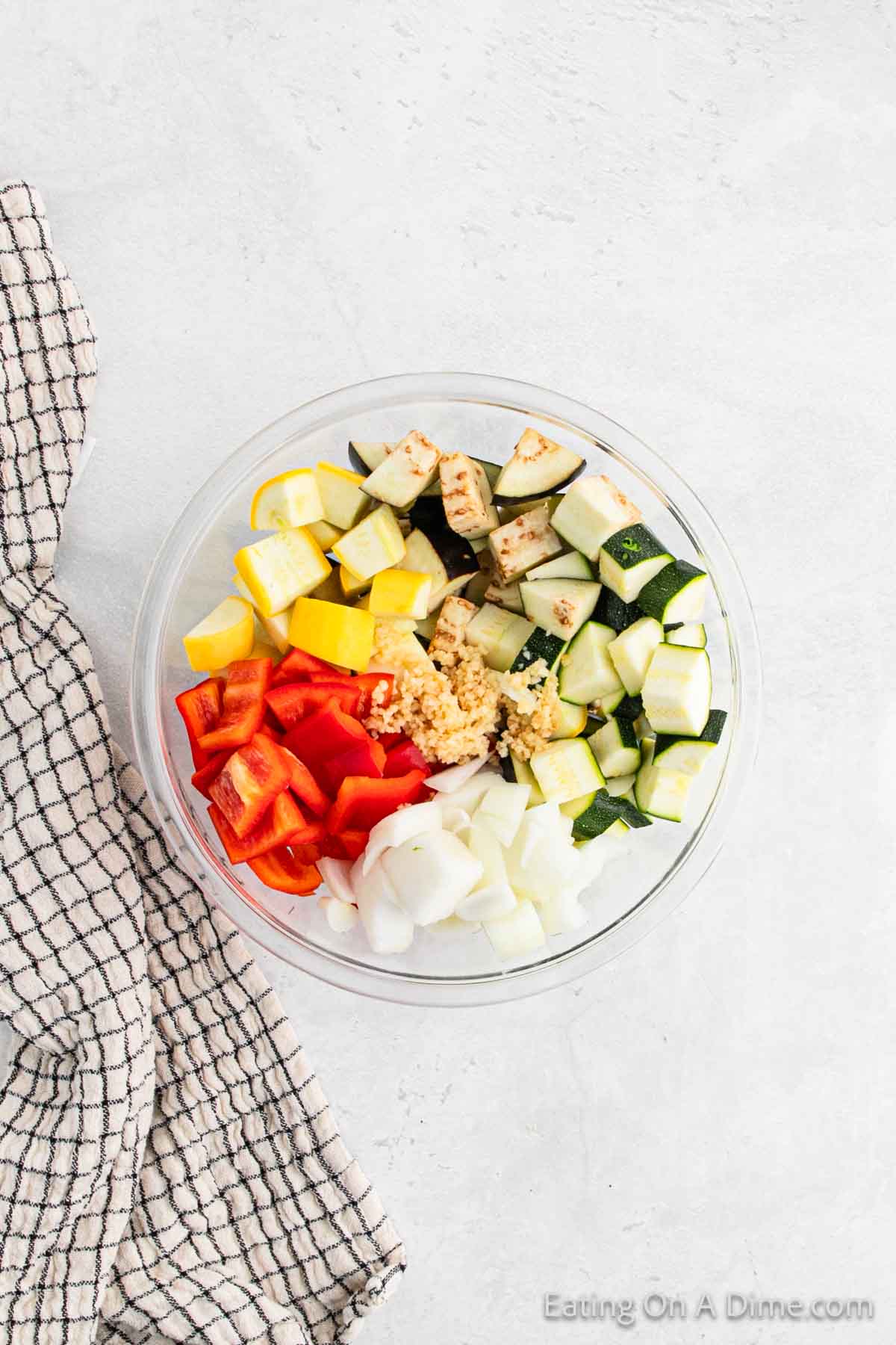 Chopped yellow squash, red bell peppers, chopped onion, and chopped zucchini in a bowl topped with minced garlic. 