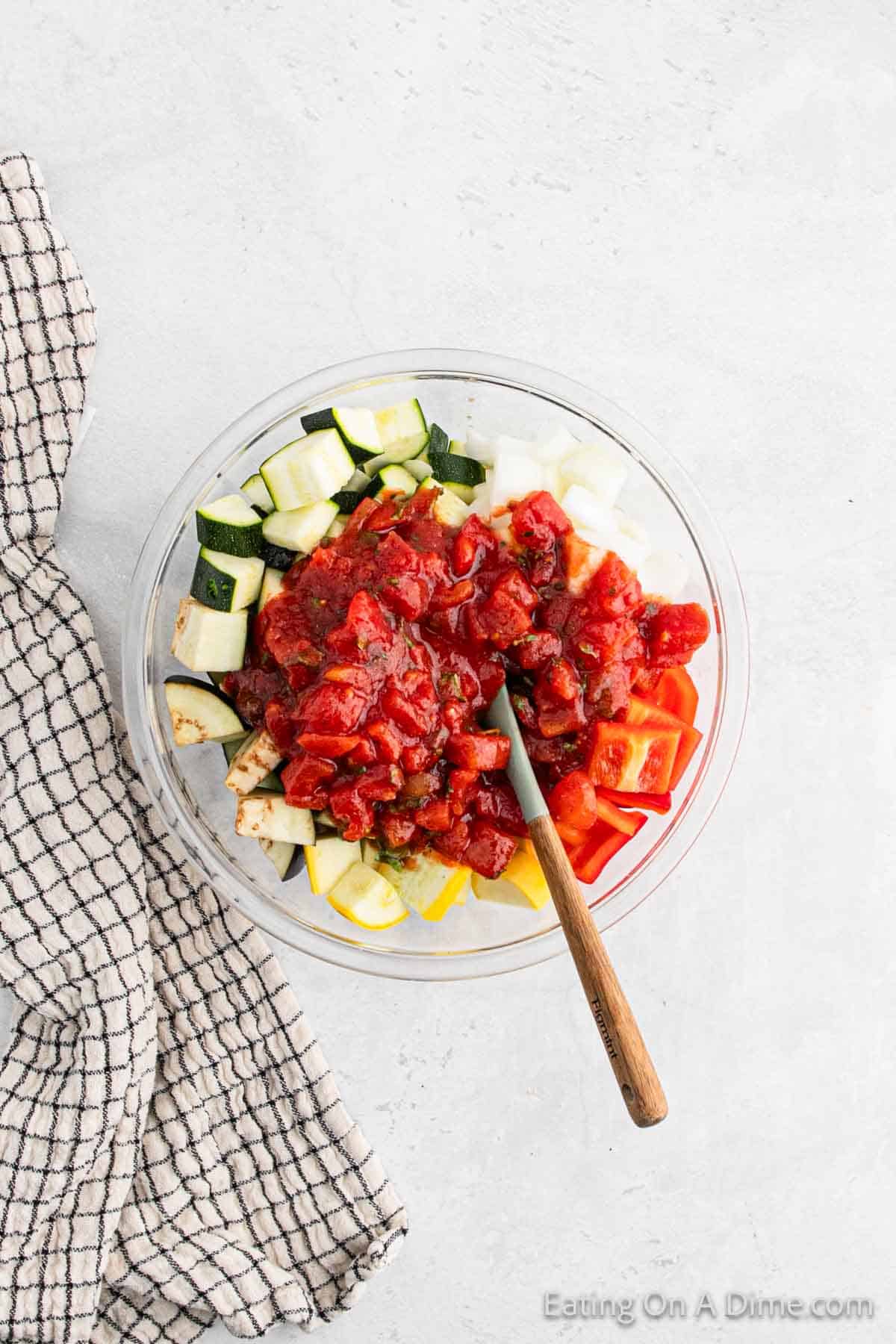 Chopped vegetables topped with tomato based sauce in a bowl with a wooden spoon