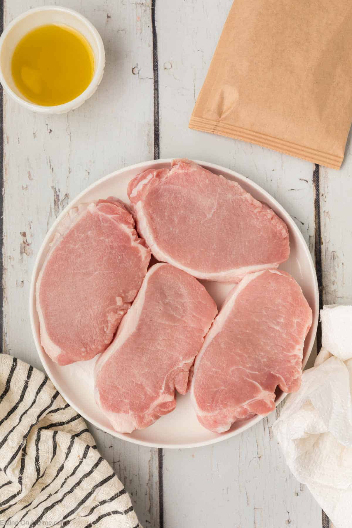 Pork Chops on a plate with a small bowl of oil and a packet of shake and seasoning packet