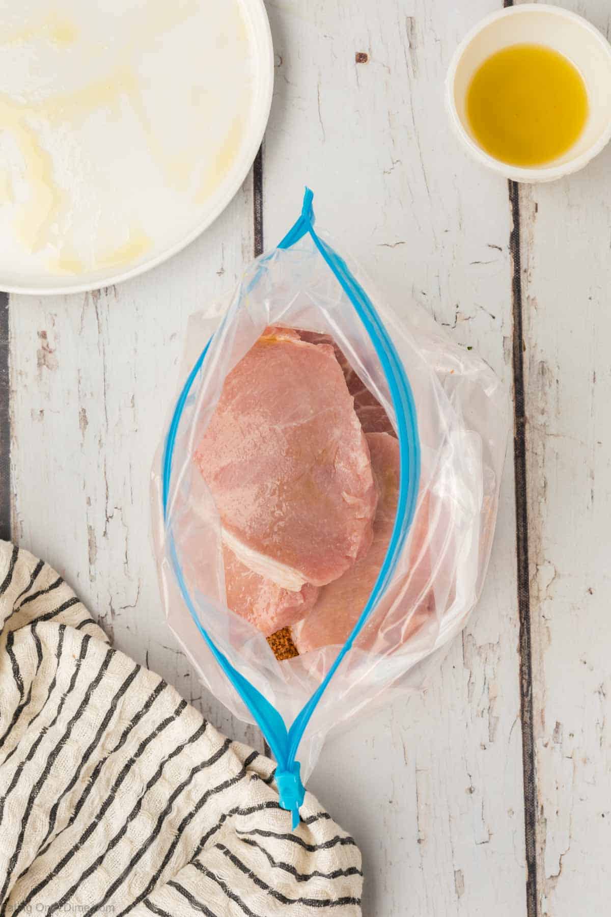 Pork chops in a ziplock bag with a white plate and a bowl of oil on the side