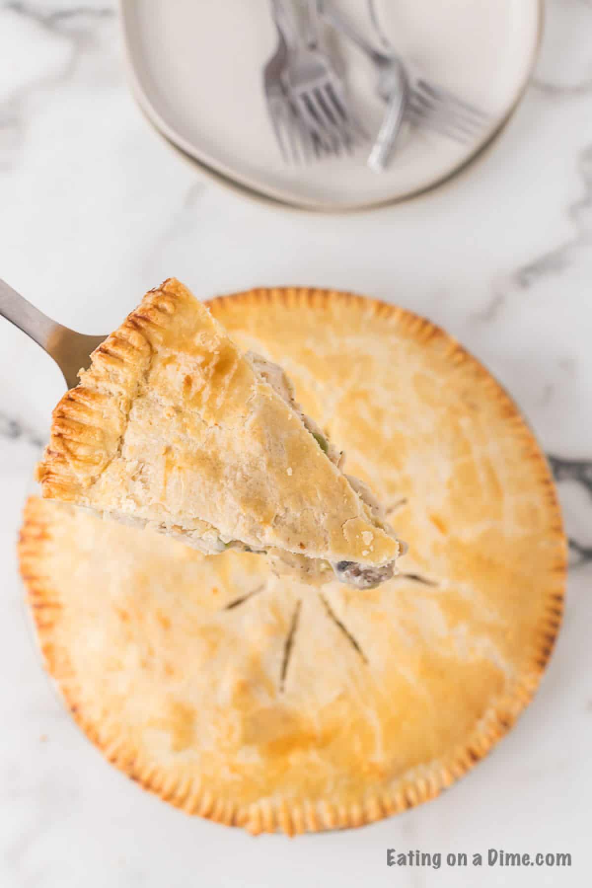 Chicken pot pie in the background with a slice of pot pie on a spatula
