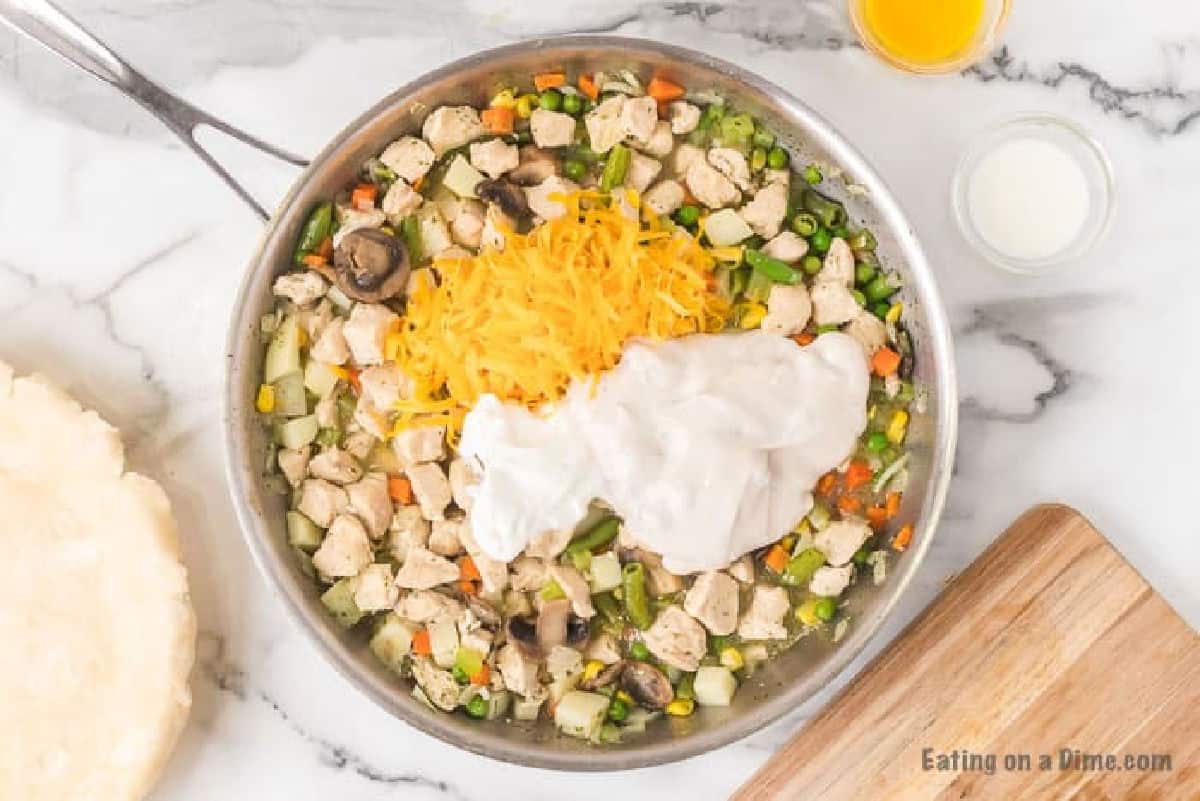 Topping the chicken and vegetables in the skillet with shredded cheese and sour cream