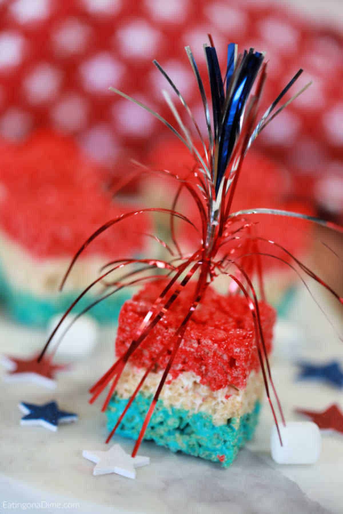 Red White and Blue Rice Krispie Treats cut into square with an red, white and blue party favor stuck into the treat