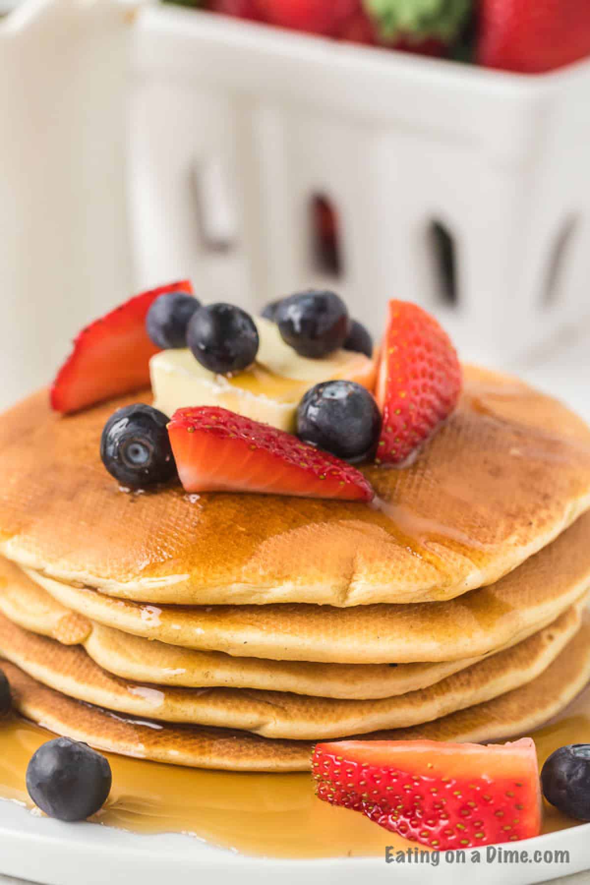 Gluten free pancakes stacked on a plate topped with butter, strawberries and blueberries and maple syrup