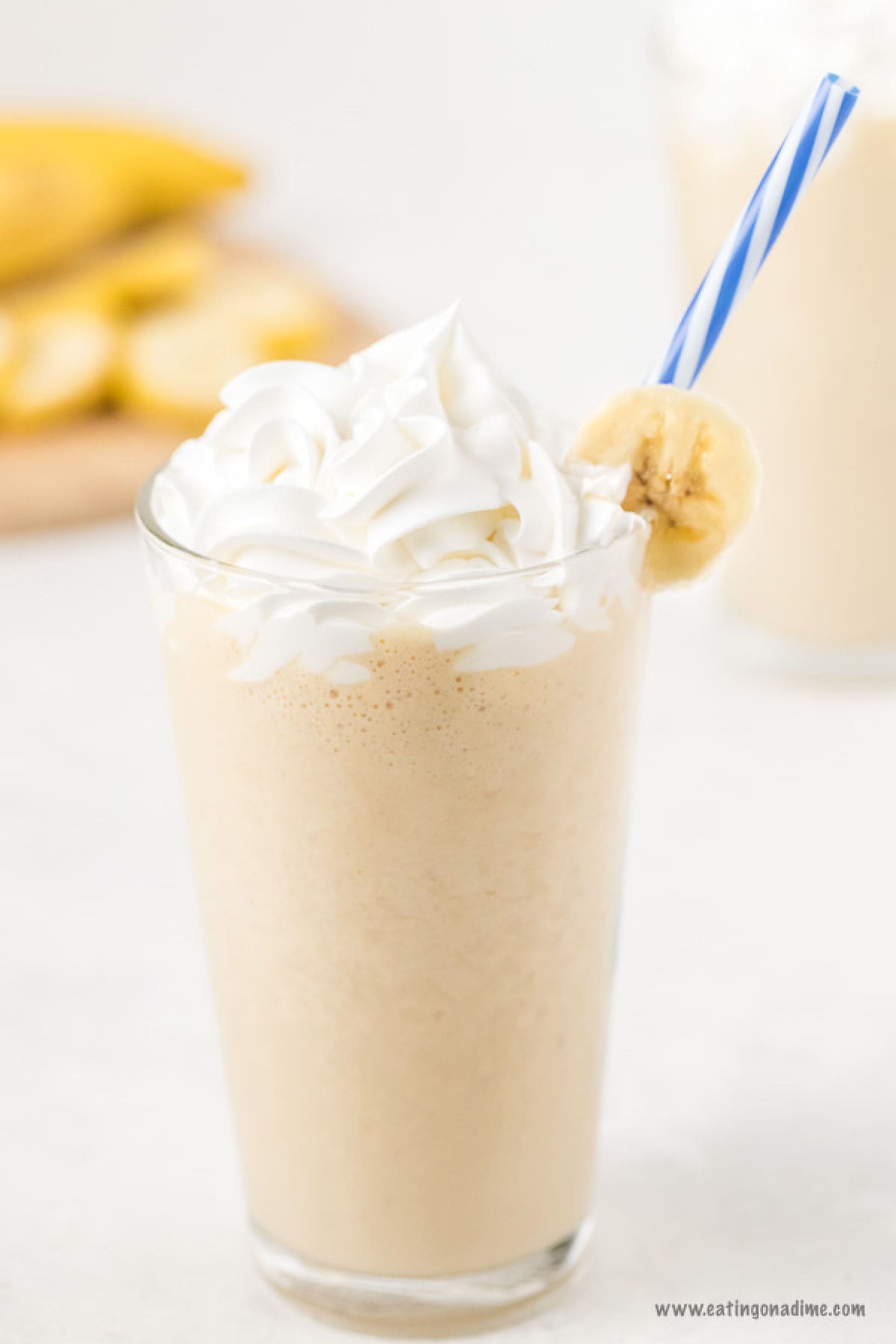 Peanut butter banana smoothie in a glass topped with a banana slice and whipped cream with a blue and white straw