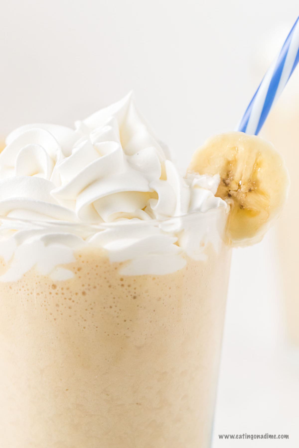 Peanut butter banana smoothie in a glass topped with a banana slice and whipped cream with a blue and white straw