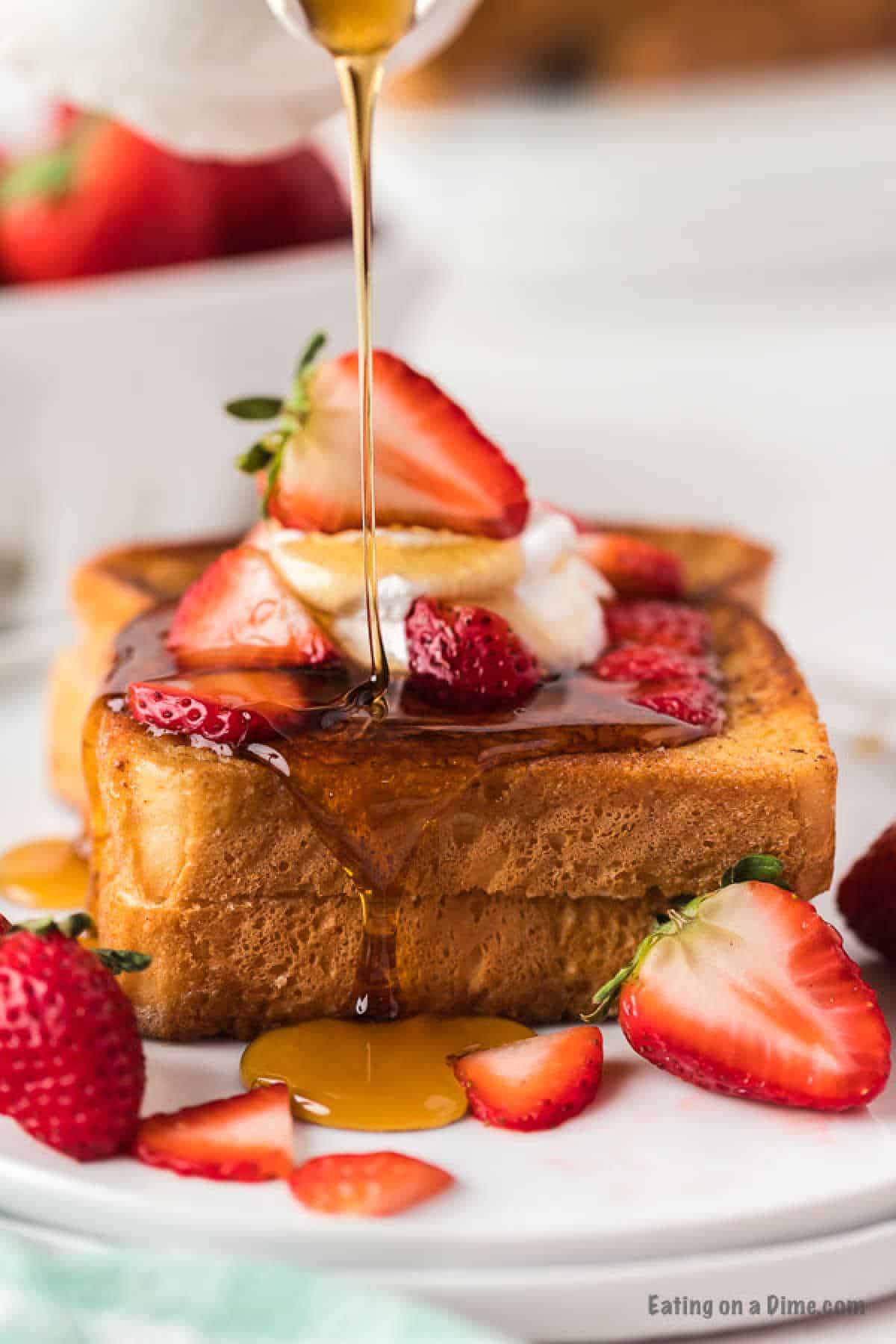 French Toast stacked and topped with fresh strawberries and maple syrup