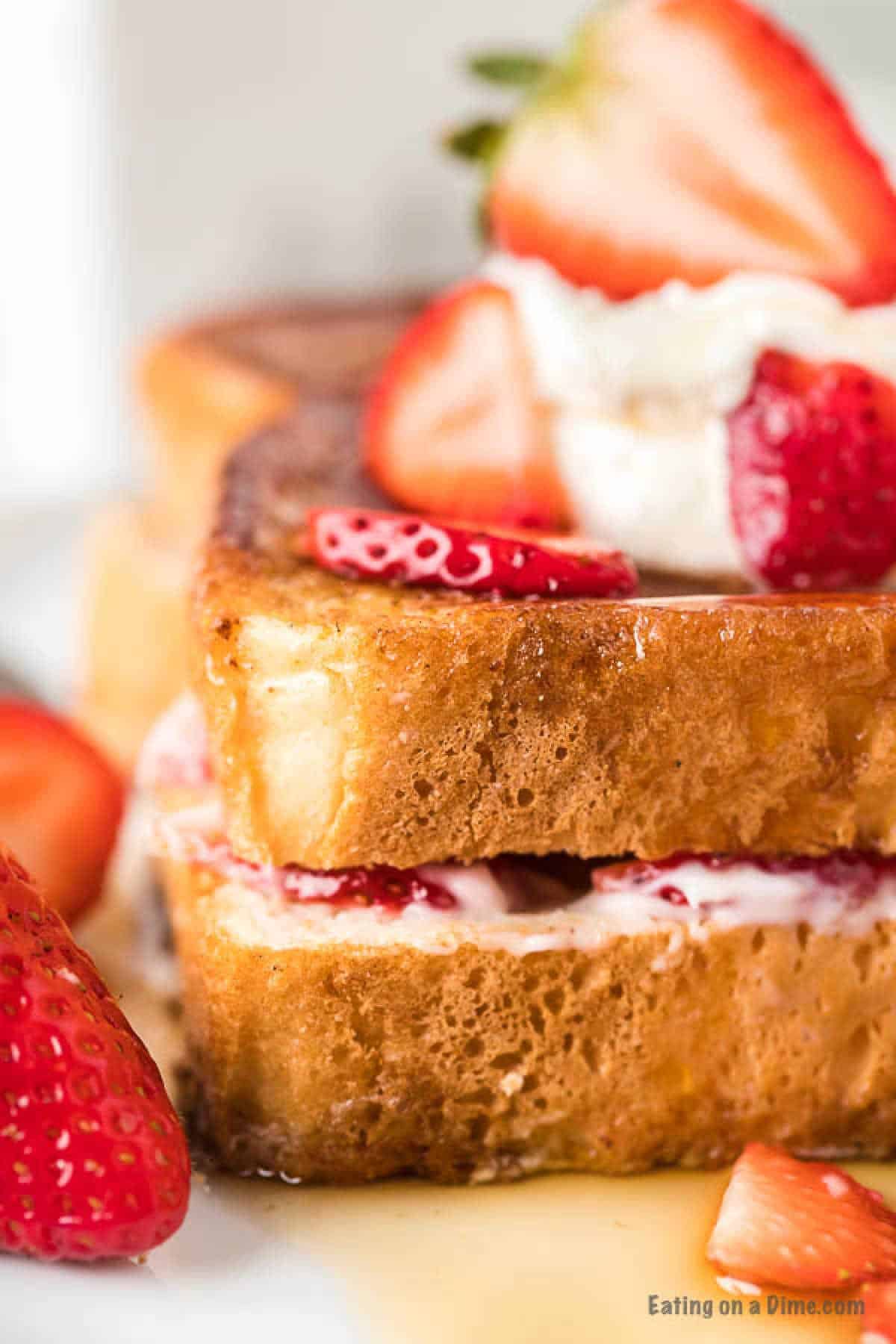 Stuffed French Toast on a plate topped with slice strawberries and maple syrup