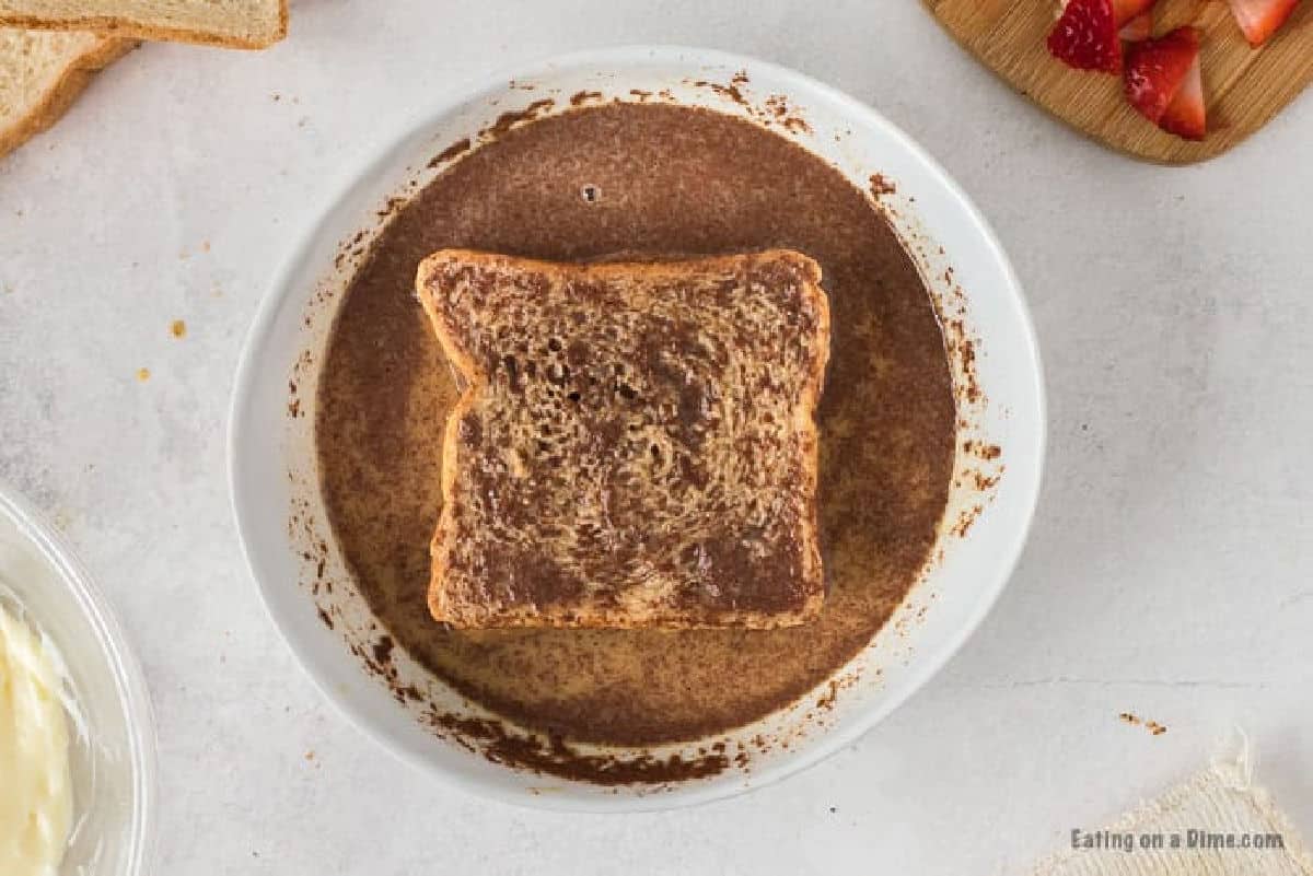 Dipping bread in the milk, cinnamon mixture in a shallow bowl
